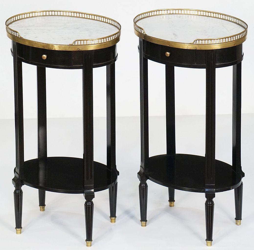 A fine pair of French black oval bedside end tables or nightstands (or night stands) in the Louis XVI Style - each side or end table made of ebonized mahogany with a Carrara marble top. The oval top framed with a pierced brass gallery, over a frieze
