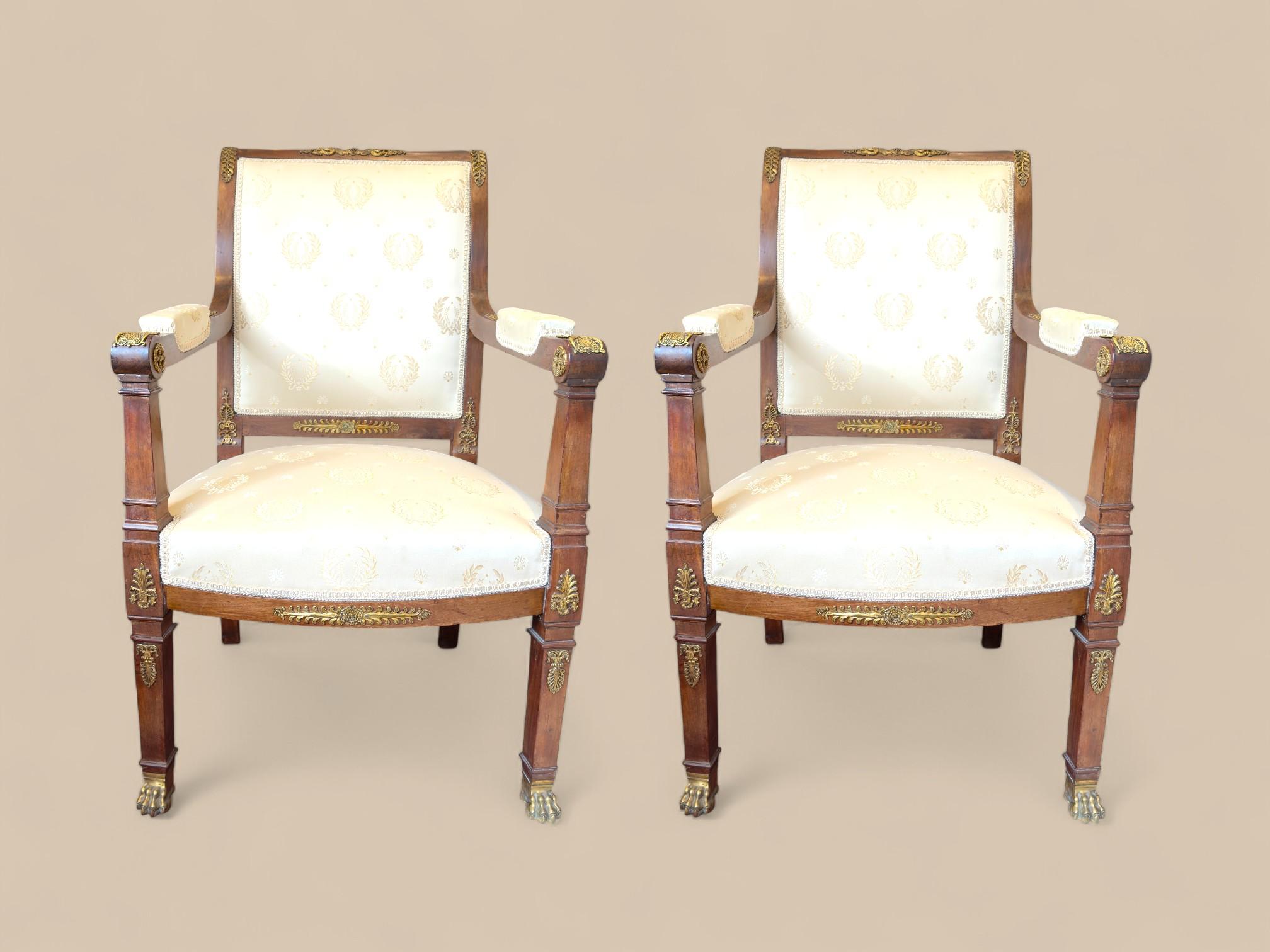Cette paire de fauteuils Empire français du début du XIXe siècle présente la symétrie, les matériaux nobles et les détails raffinés caractéristiques de l'époque. Fabriquée en bois massif richement teinté, chaque chaise présente des pieds avant