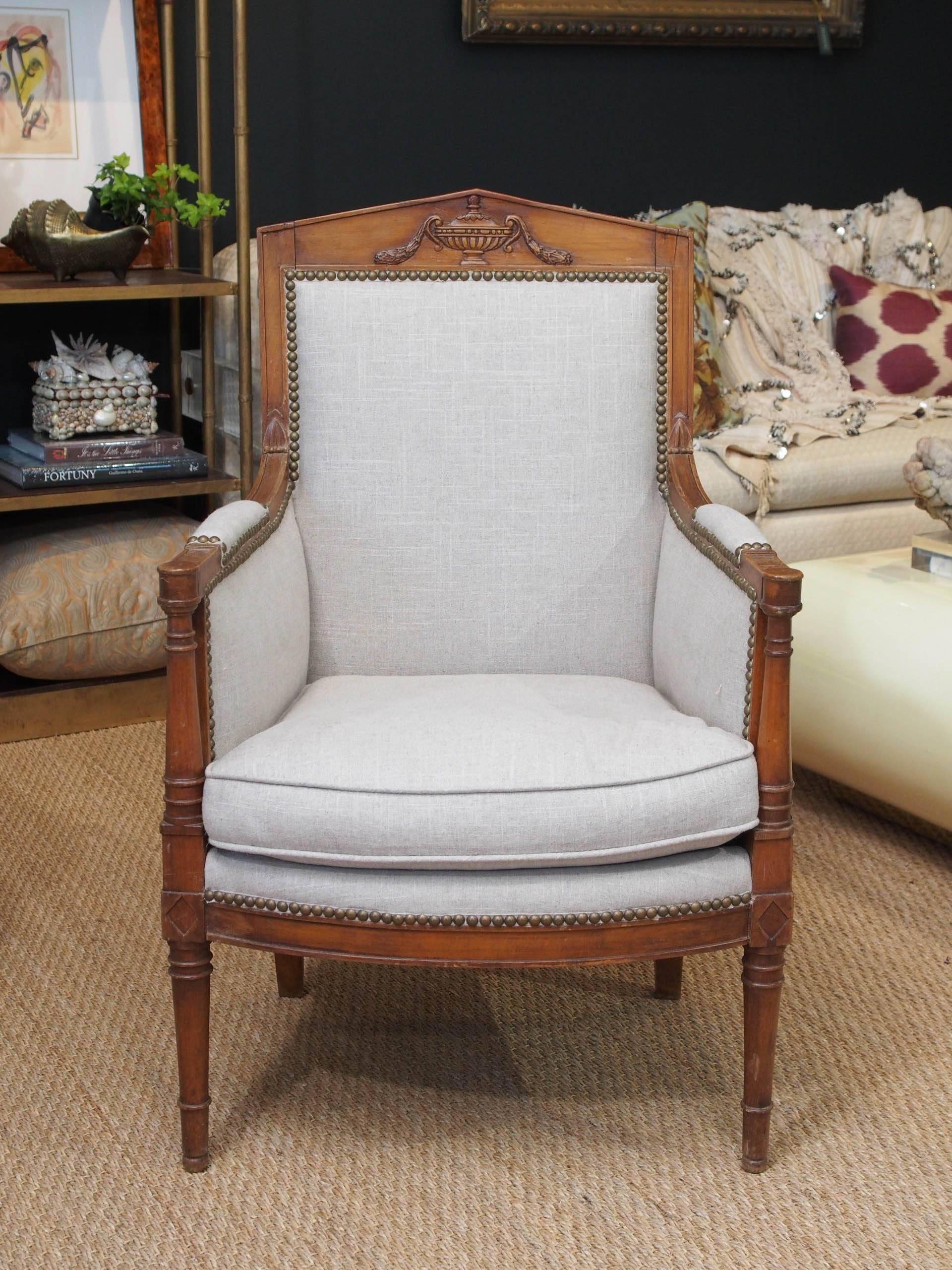 Pair of French Empire walnut bergère chairs covered in neutral linen with nailhead trim.