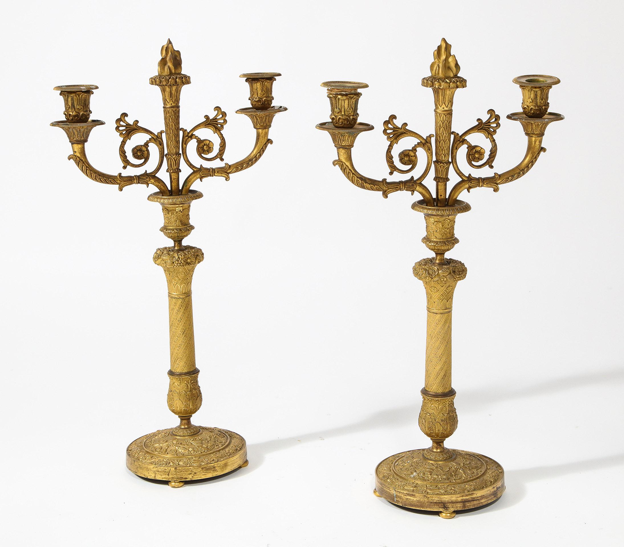 Con una fiamma centrale rimovibile in bronzo affiancata da candelabri stilizzati, su un gambo in rilievo con base simile.