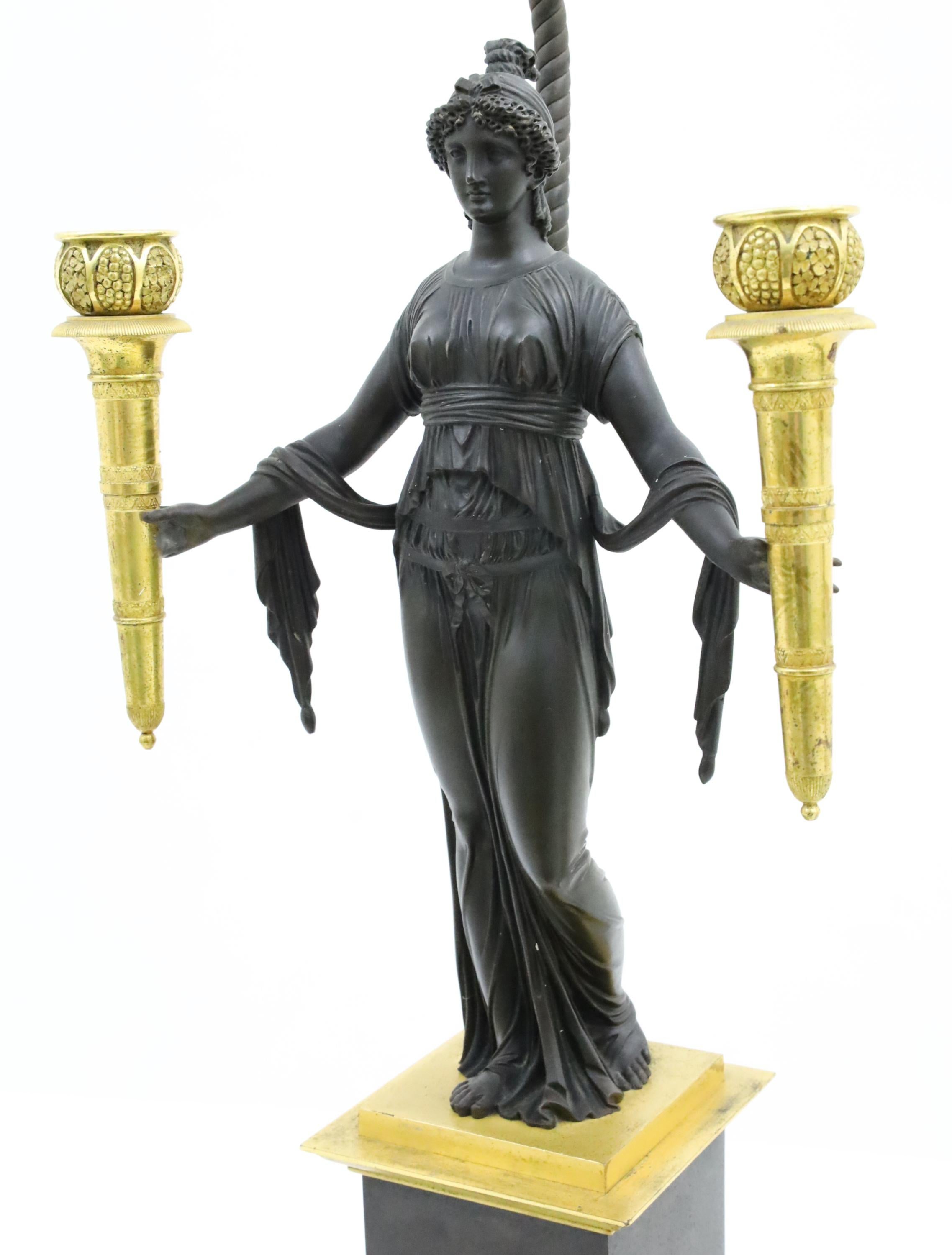 Pair of French Empire bronze candelabra having female attendants in flowing gowns holding gilded torchieres, standing on parcel gilt plinths, 19th century, now mounted as lamps