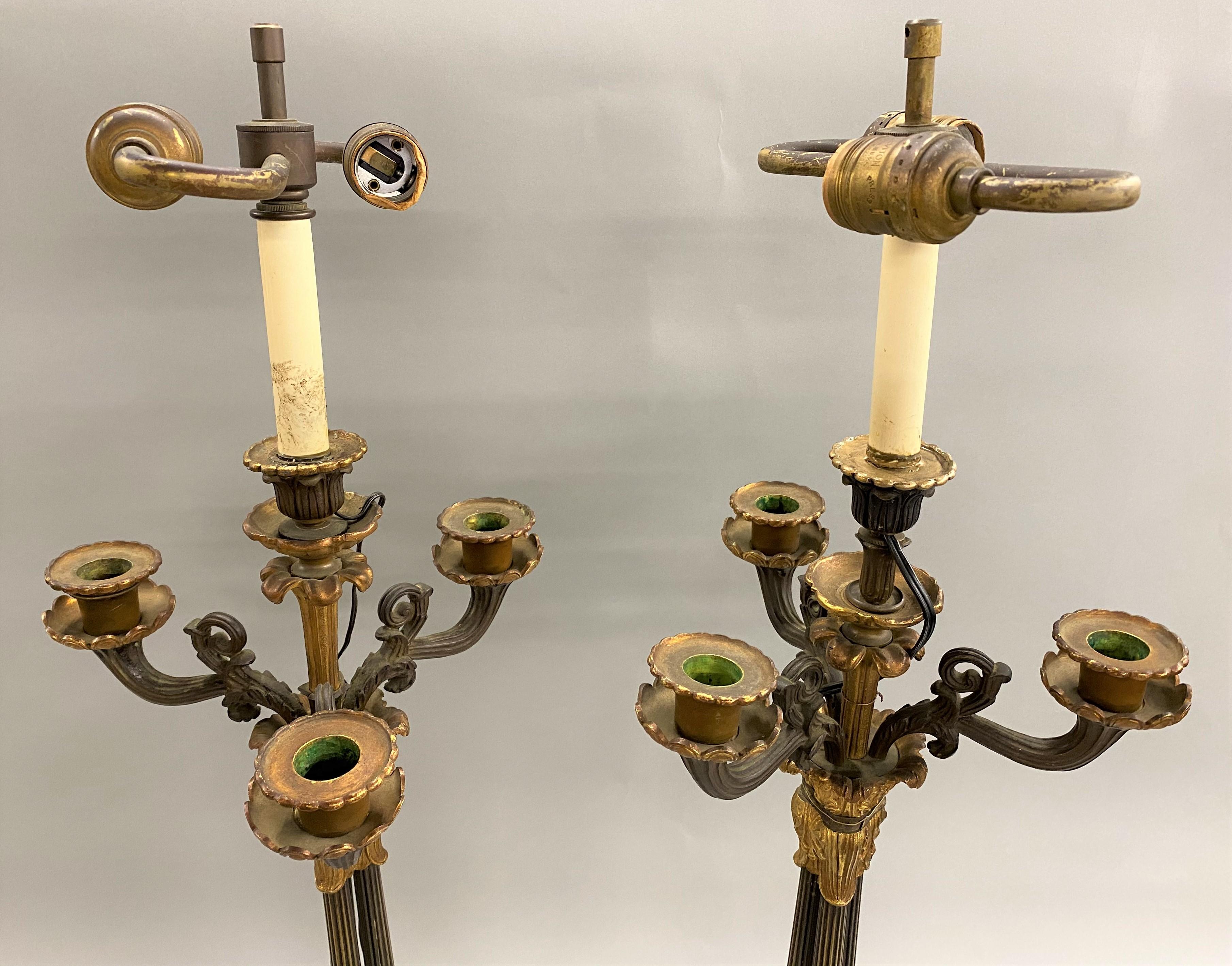 A fine pair of French Empire two-light bronze candelabra lamps with three candle arms, gilt foliate ormolu, each with triple reeded column stems on foliate tripod base highlighted with gilt ormolu and felted bases. The pair dates to the early 19th