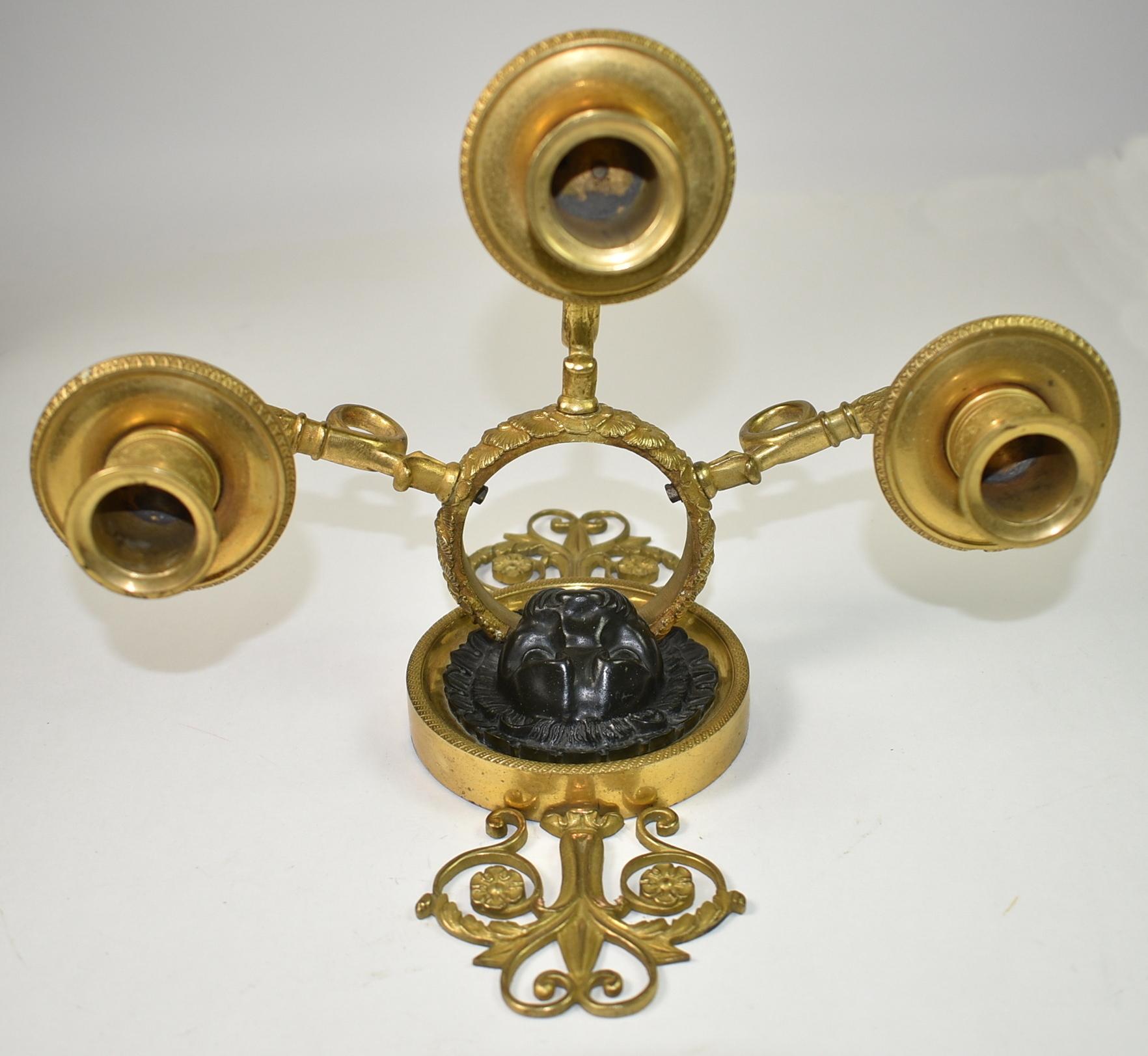 Pair of French Empire bronze wall sconces. Circa 1890's. Bronze sconces with gold tone finish. Central lionhead with each and 3 extended candle arms. Good condition, a chipped bobeche and a disfigured heart on the top of one as shown in photos.