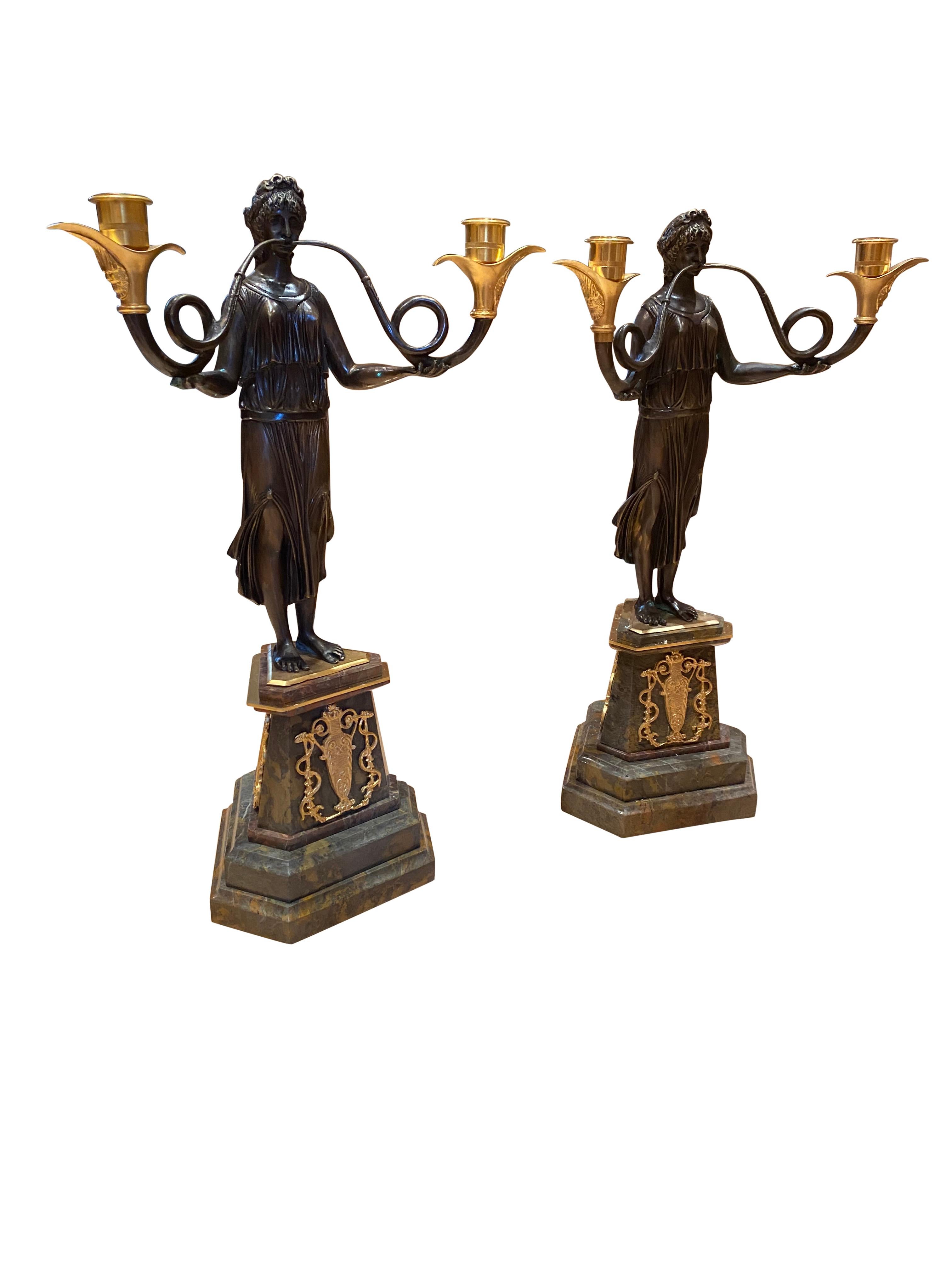 Pair of French Empire candelabras on marble bases, 20th century. Perfect left and right, each maiden holds aloft the two Ormolu candle branches. Stands on the two tone marble base which is smooth and chip free. Further Ormolu fixtures on the base