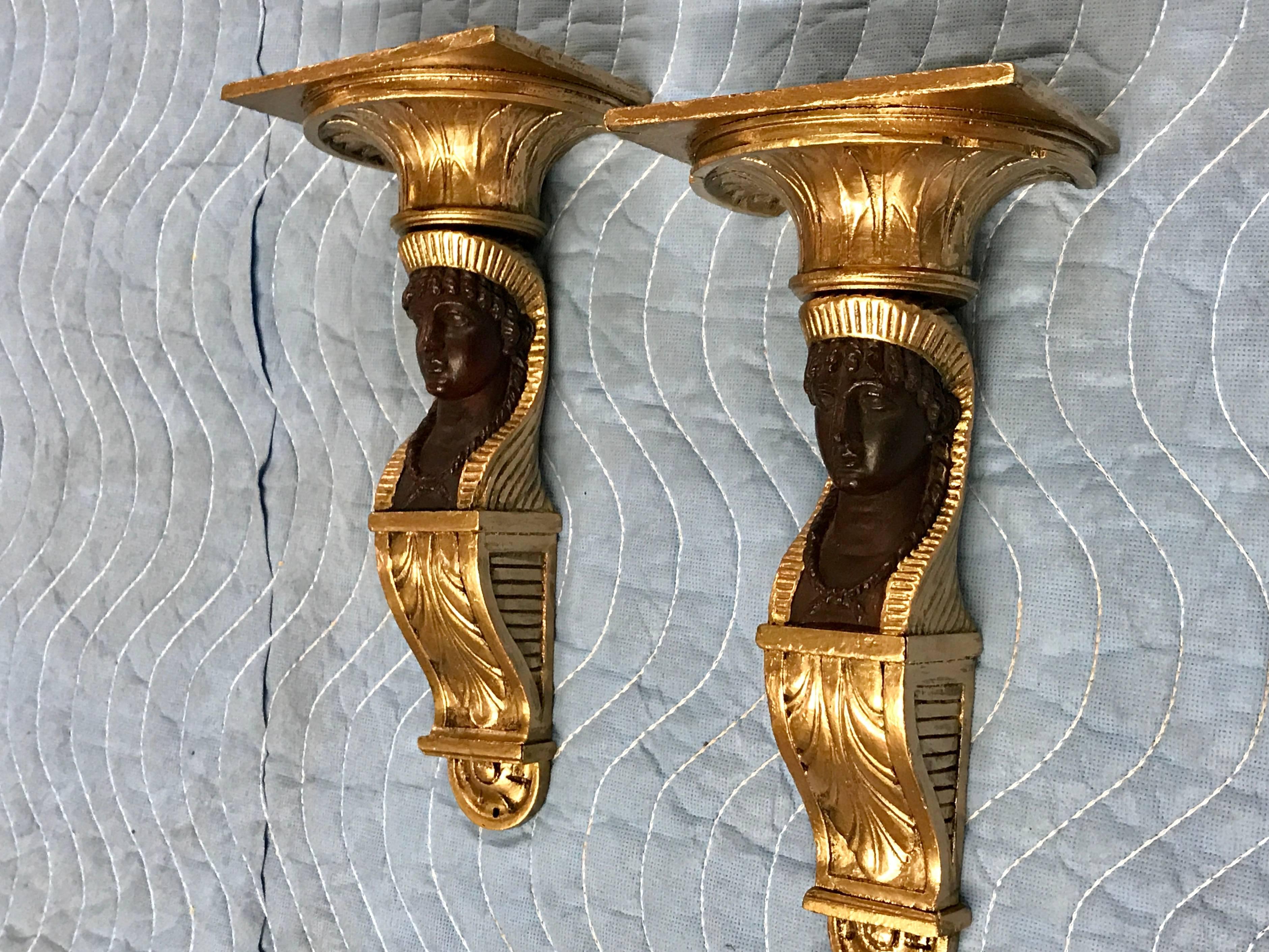 A pair of French empire Egyptian motif wall brackets, each one figural carved giltwood and mahogany with anthemion details.