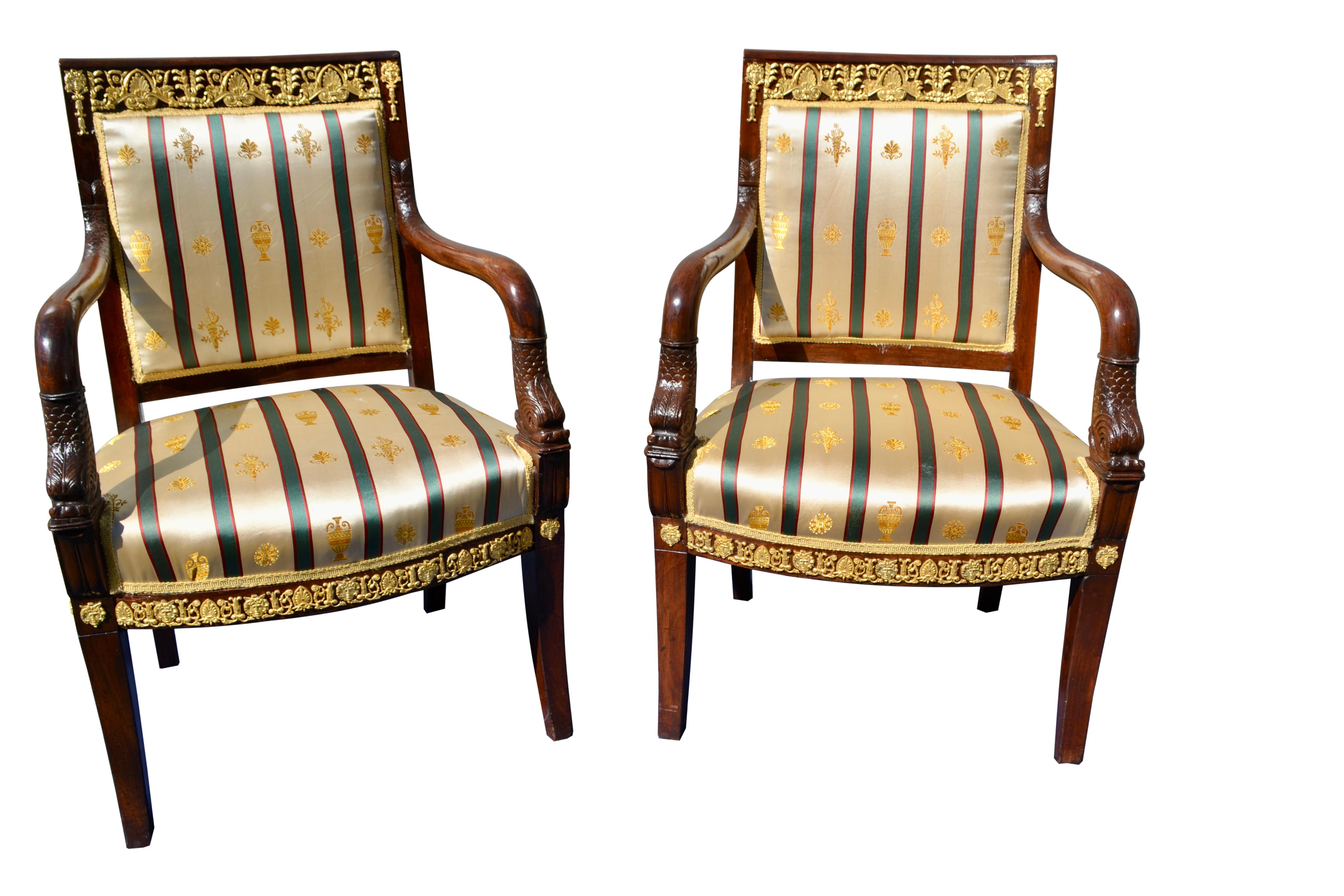 A striking pair of late French Empire mahogany armchairs, highly decorated with gilded bronze mounts on the upper back rail and all round the bottom of the seat as well. The curved open front arms terminate in carved dolphins. The chairs have been