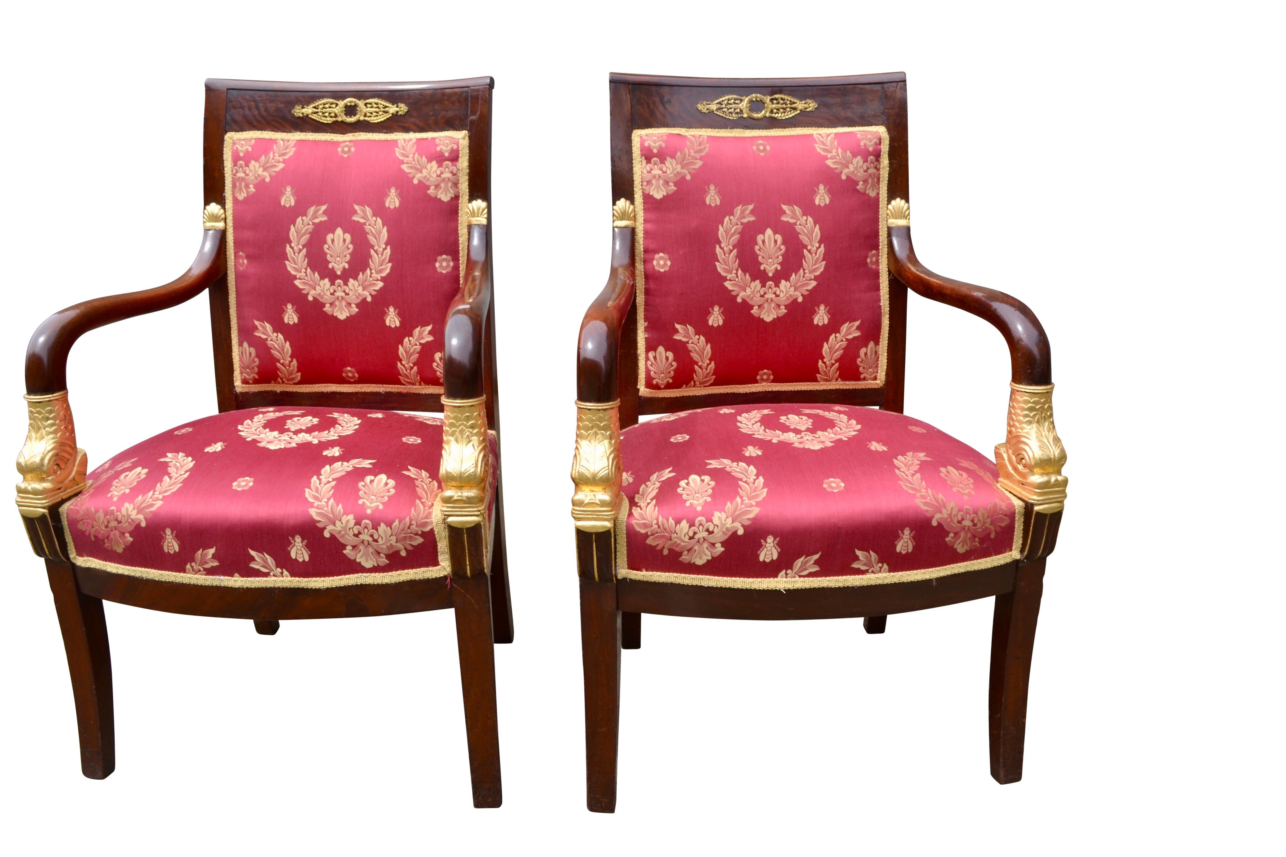A fine pair of period French Empire arm chairs. The mahogany frames are accented with gilded bronze mounts but most strikingly the swept open arms terminate in beautifully carved gilded wood dolphins. The top of the arms joining the square backs
