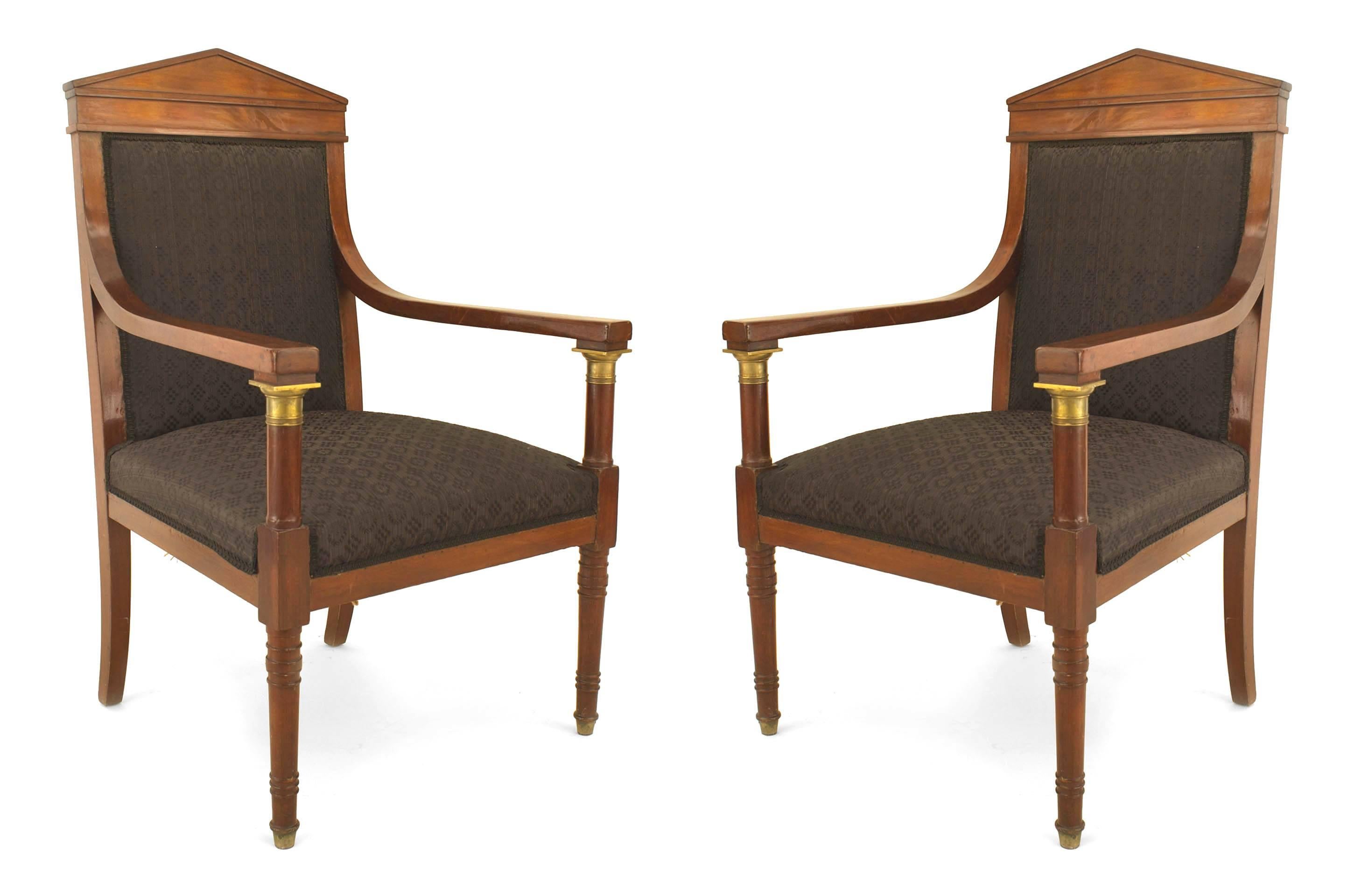 PAIR of French Empire (19th C) mahogany open arm chairs with a pediment back & black upholstery having arms supported by bronze mounted columns and supported on turned front & saber rear legs.
