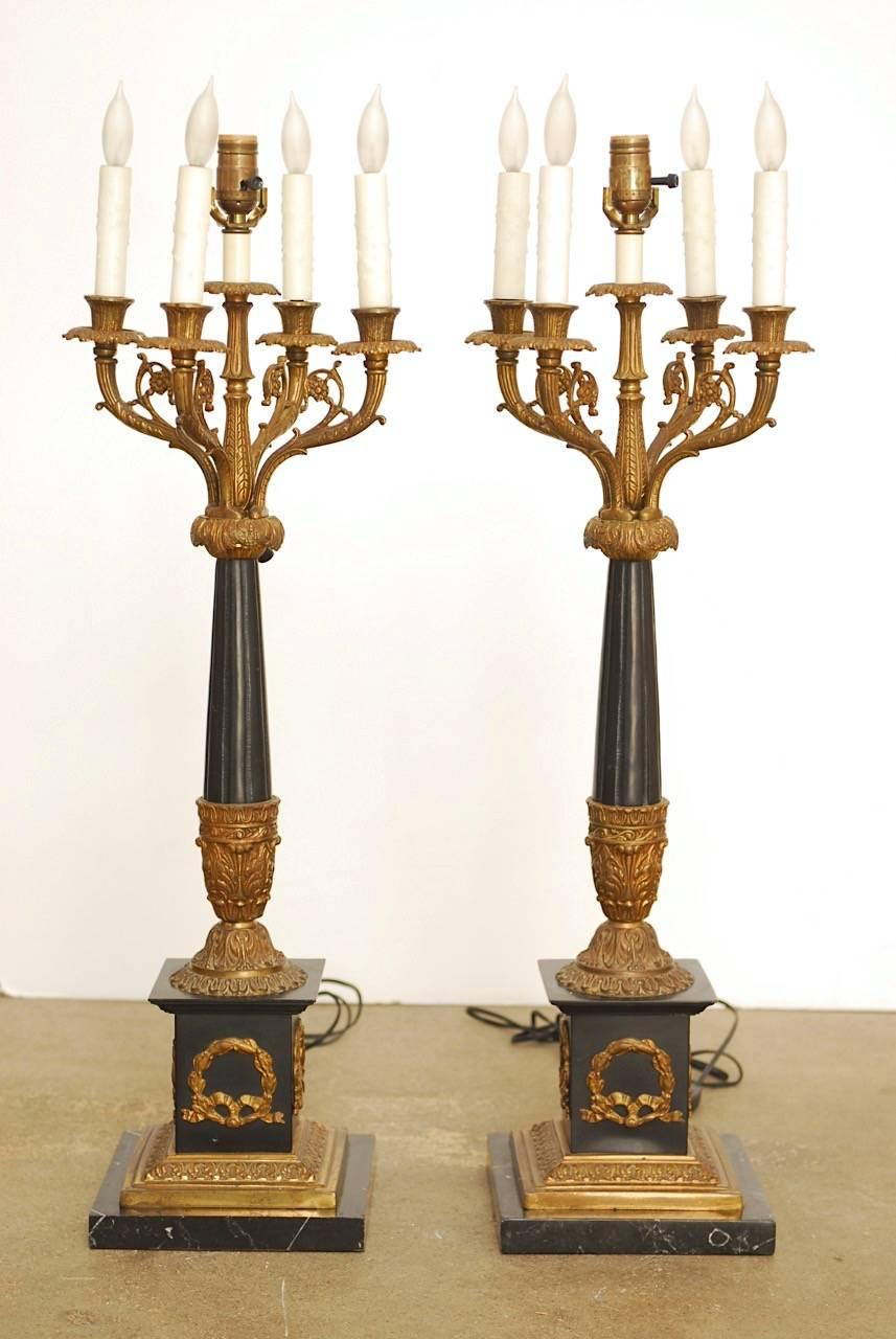 Magnificent pair of neoclassical candelabras converted to table lamps made in the French empire taste. Features a square marble base surmounted by a black and gilt decorated square column. The four arm candelabra is centred by a light that works on