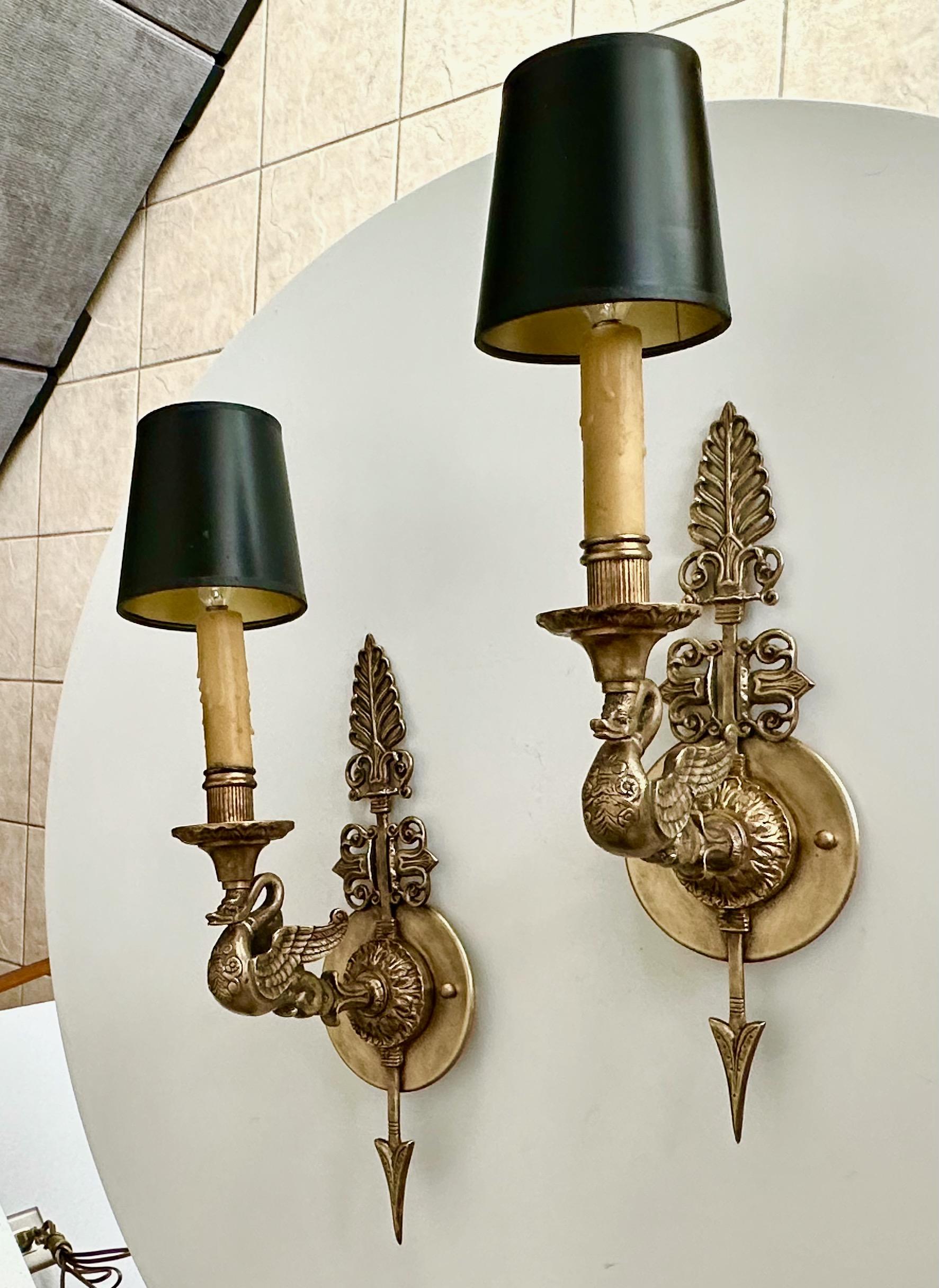 Pair of antique French Empire style brass wall sconces. Nicely executed with fine detailing including arrow and swan motif. Each sconce uses single candelabra base bulb. Shades included. Height of sconce without shade 15