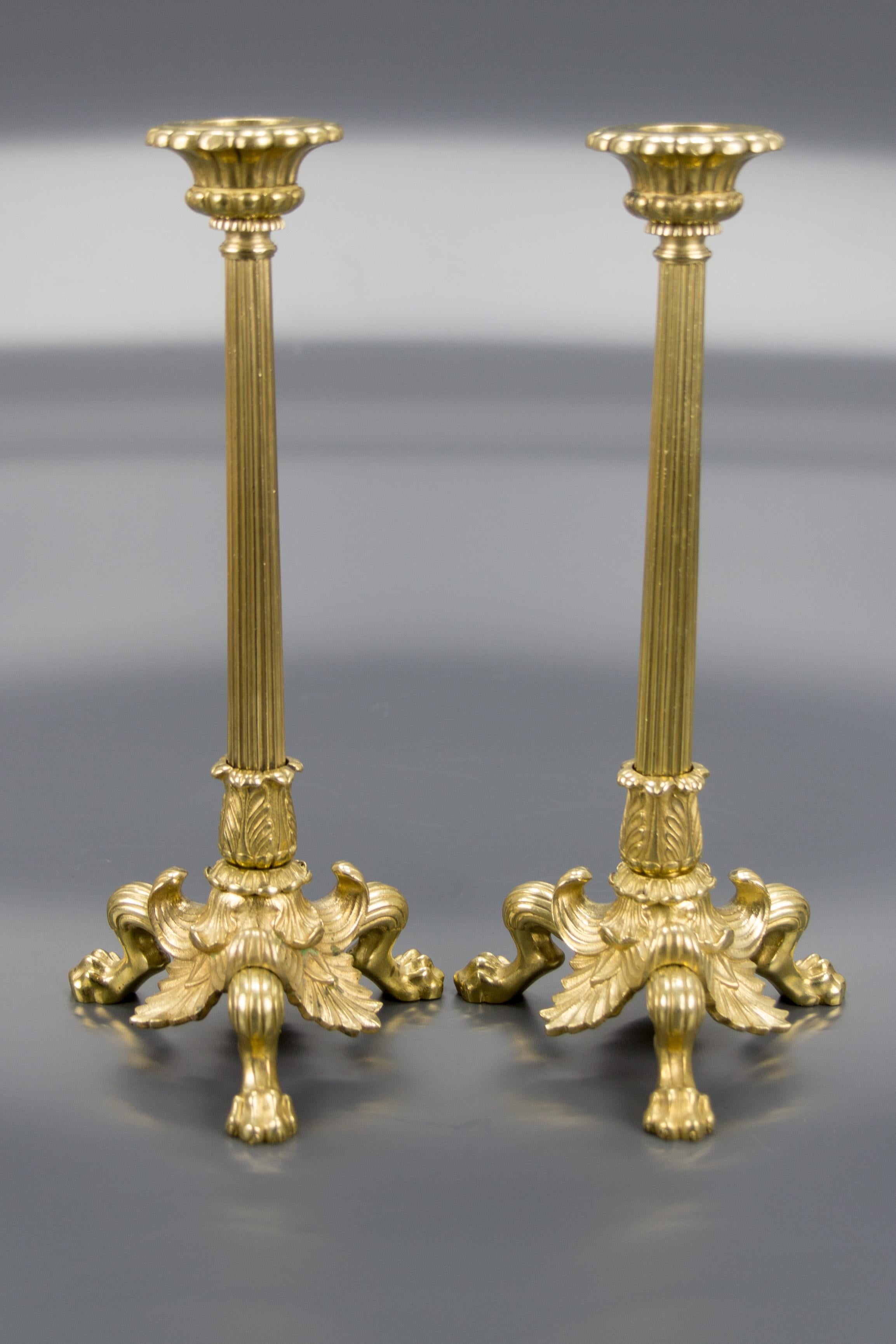 A beautiful pair of French Empire style bronze and brass candlesticks. Each candlestick features a fluted columnar stem, ornate collar, and is raised on three elaborately leaf-capped lion paws. These elegant antique candlesticks make a wonderful