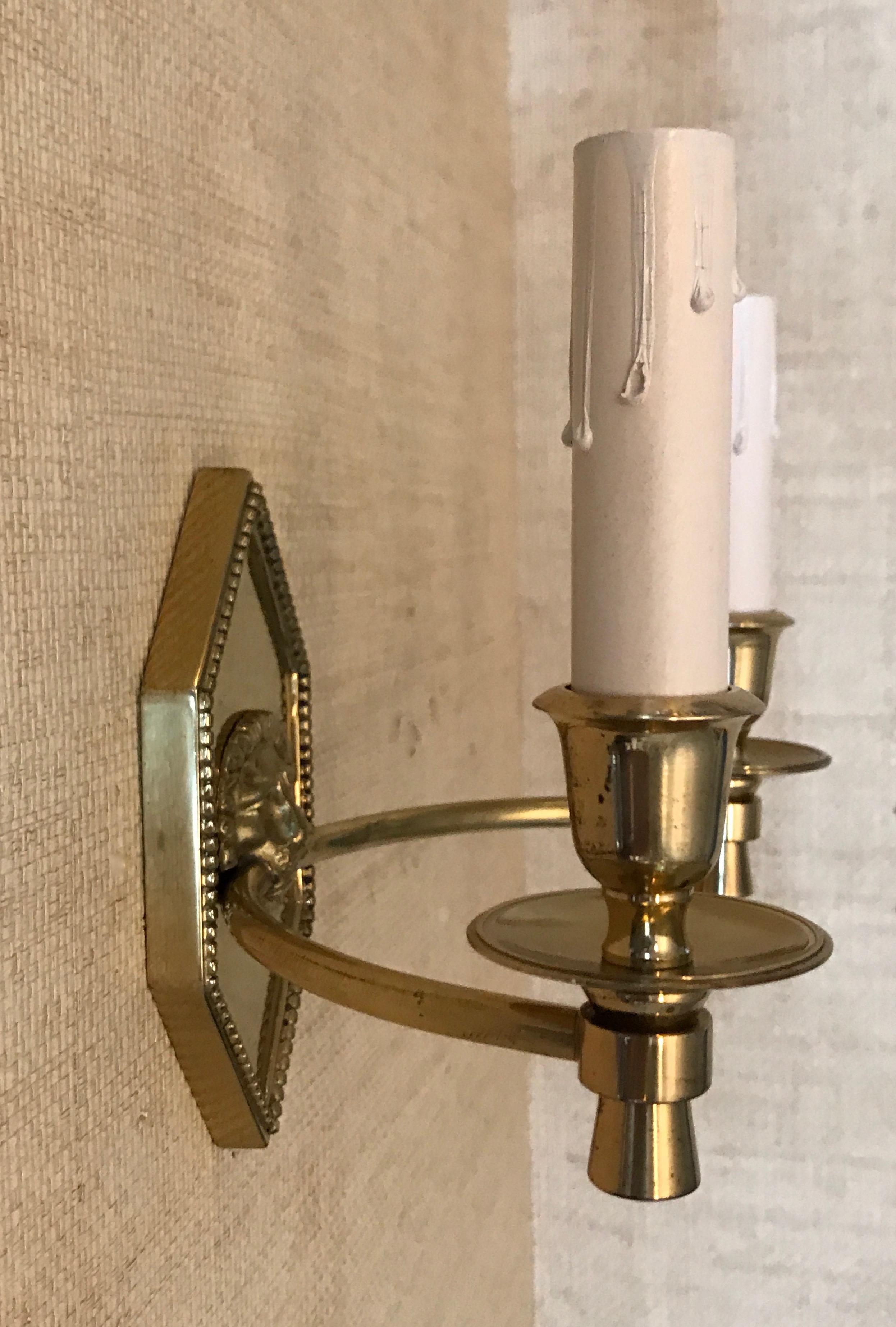 Pair of delicate French Empire style brass wall sconces with double arms on elongated hexagonal backplates with beaded detail and central lion motif. Rewired from US installations, each sconce uses 2 - 40 watt max incandescent bulbs or any wattage
