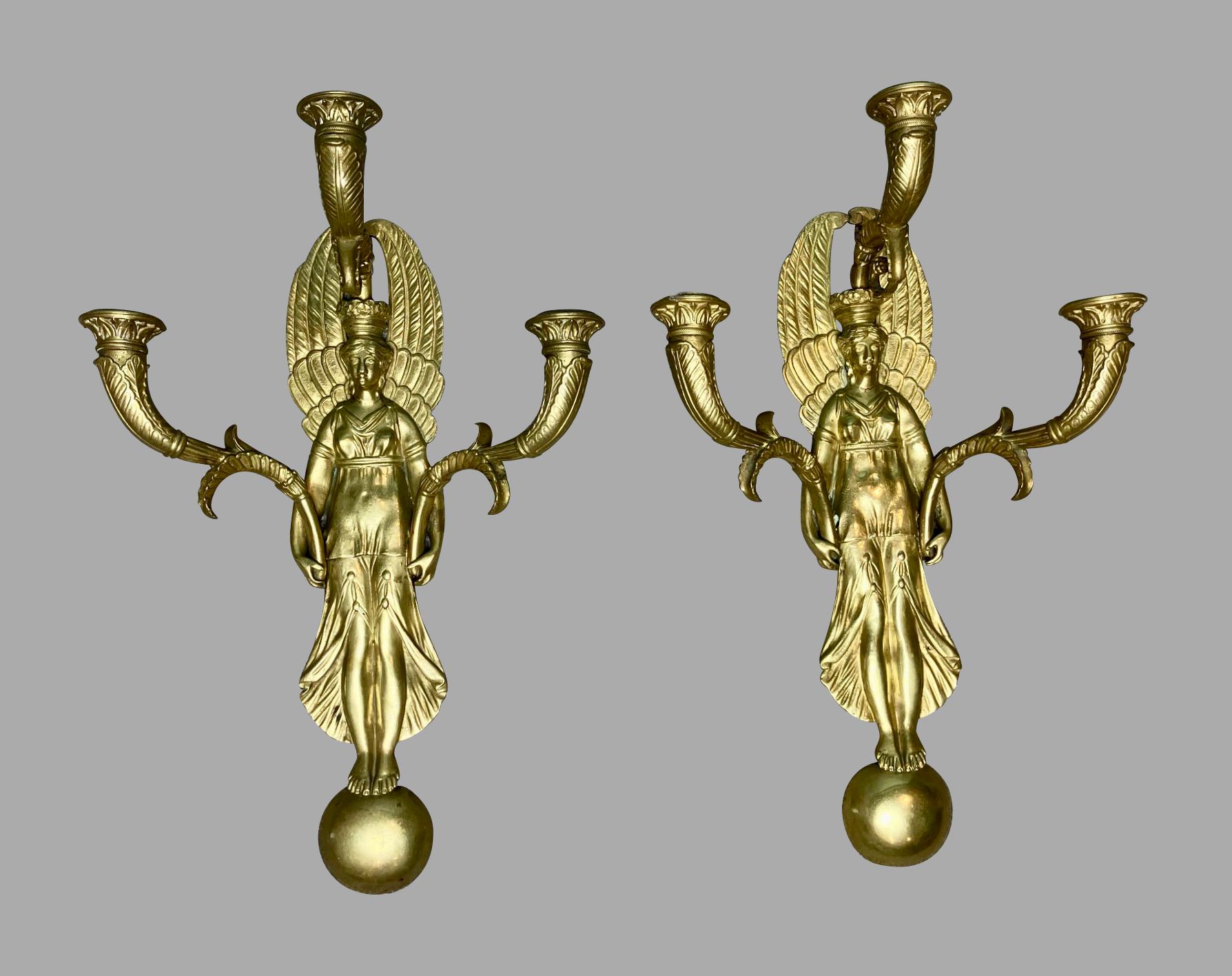 A well-cast and stylish pair of French brass or bronze 3 light wall sconces in the Empire style, each with a central female figure garbed in classical clothing and holding 2 candle branches while wearing a third central branch as a crown. She rests