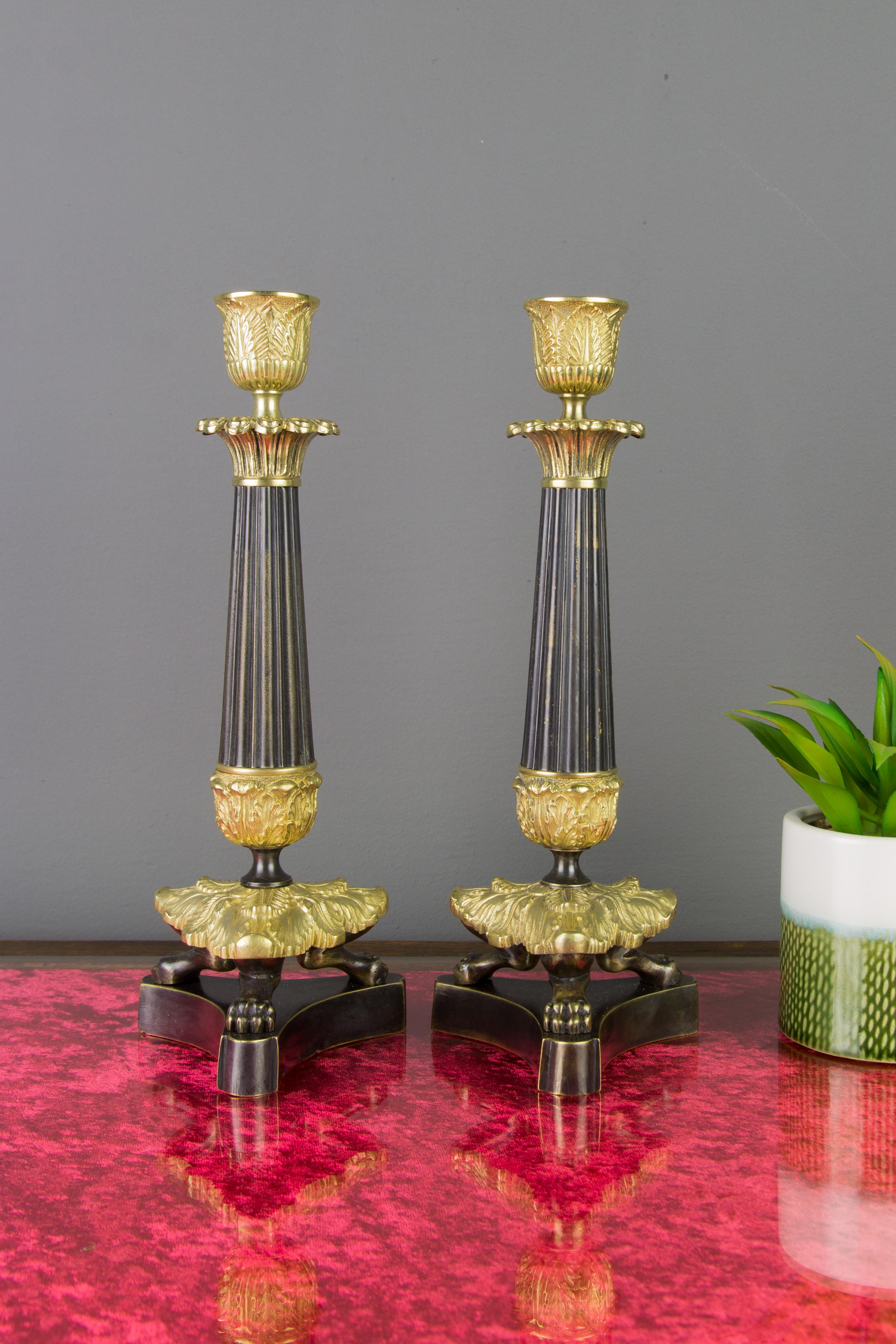 Sehr schönes Paar französischer Kerzenständer im Empire-Stil aus patinierter Bronze und Messing. Jeder Leuchter hat einen kannelierten Säulenstiel, einen mit Blättern verzierten Kragen und steht auf drei kunstvoll mit Blättern bedeckten