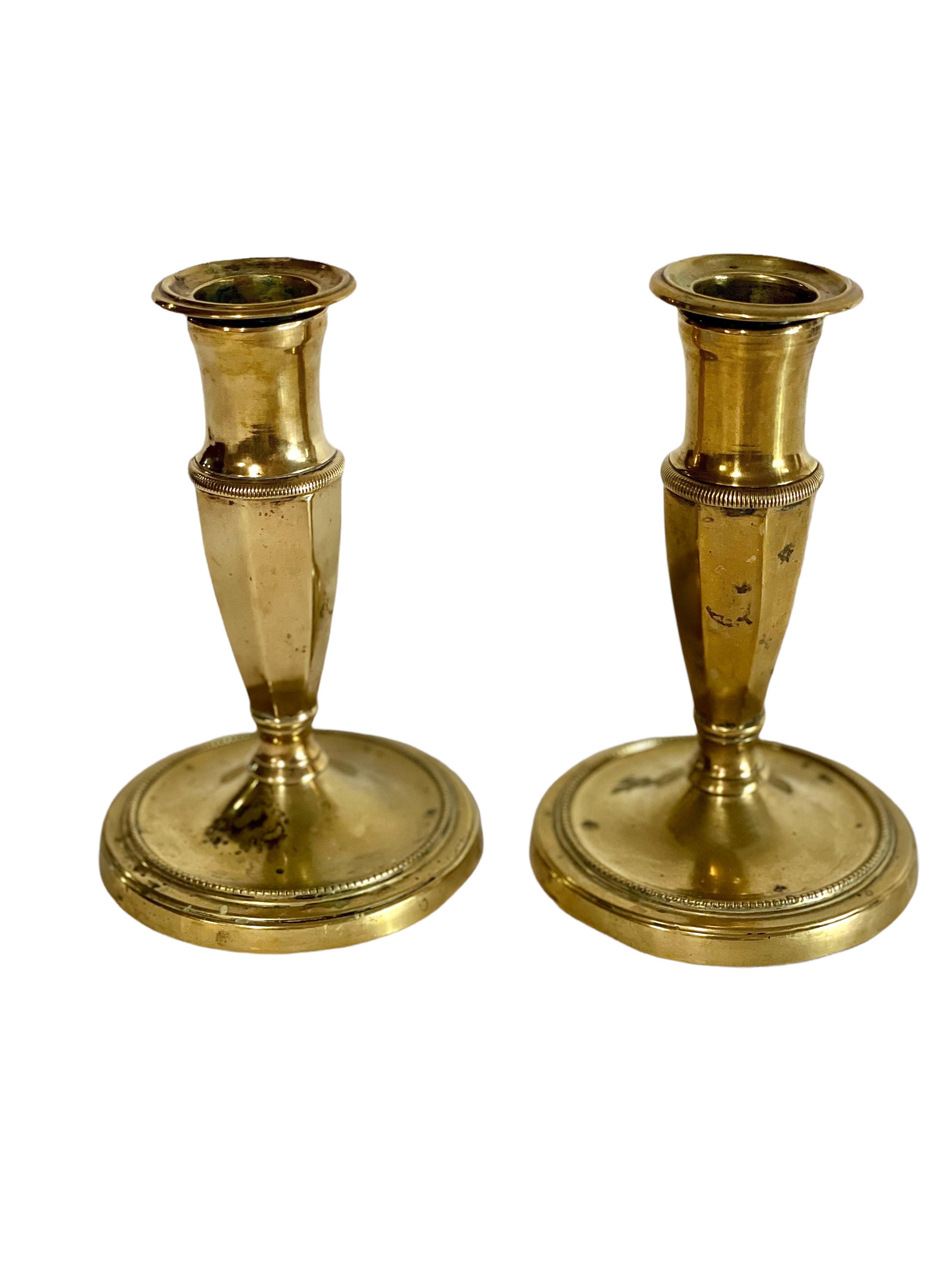 An attractive and very smart pair of French Empire style bronze candlesticks. Their compact size would have made them ideal for travelling. Circular bases, with concentric ring decoration support an elegantly simple and planed stem and candle cup.