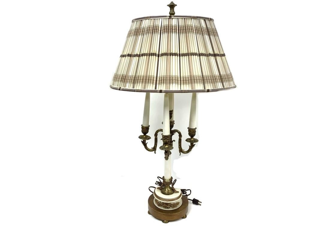 Pair of vintage French Empire style candelabra lamps with four leafy scrolled brass arms having wooden paint decorated faux candles. 
The twin light lamps with a switch behind the demilune form white marble bases with applied metal leafy motifs. The