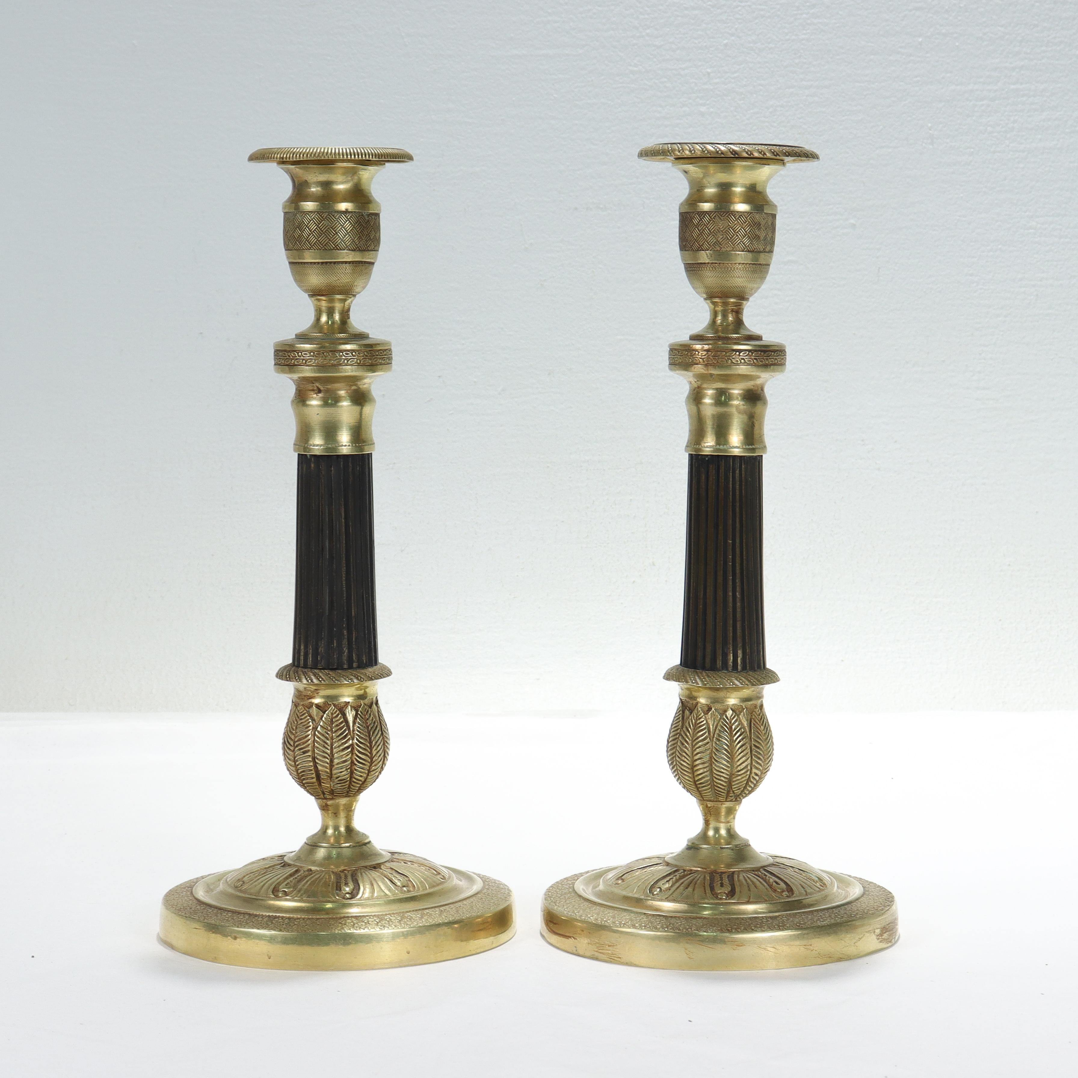 A fine pair of French Empire gilt bronze candlesticks.

With intricate raised decoration in the form of geometric and foliate patterns.

The middle of each candlestick is fluted and has a warm brown patina.

The bobeches are removable and the
