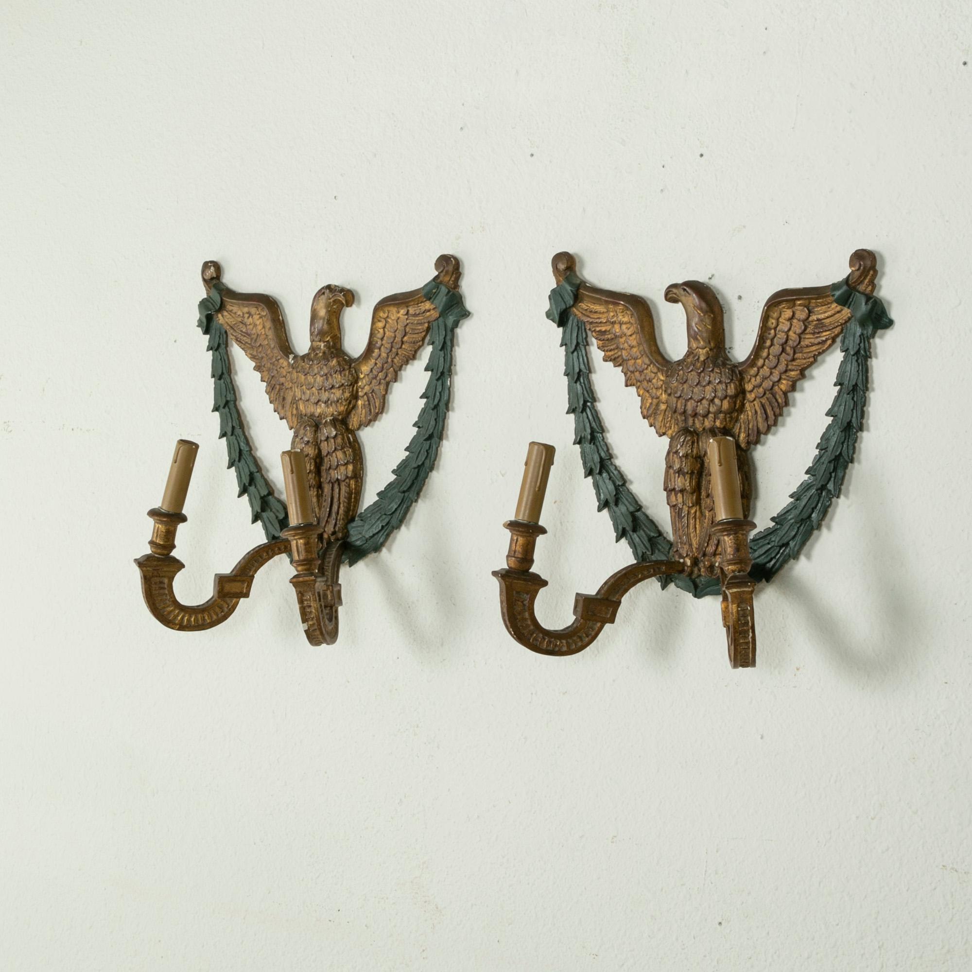 At almost 18 inches in height, this pair of French Empire style gilt wood sconces from the turn of the twentieth century features opposing Napoleonic eagles holding laurels in their talons. Each sconce has two arms for lights. Wired to American