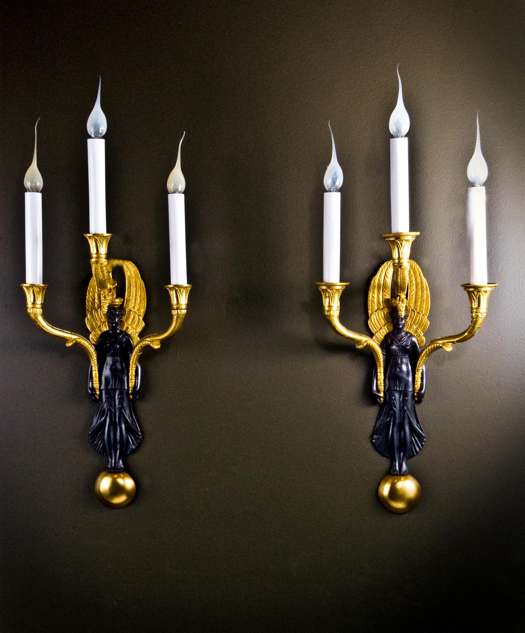 A grand and finely cast pair of French Empire style ormolu and patinated bronze three-arm figural wall sconces. Each sconce centers on a striking classical maiden, beautifully rendered in dark patinated bronze and draped in flowing robes, her head