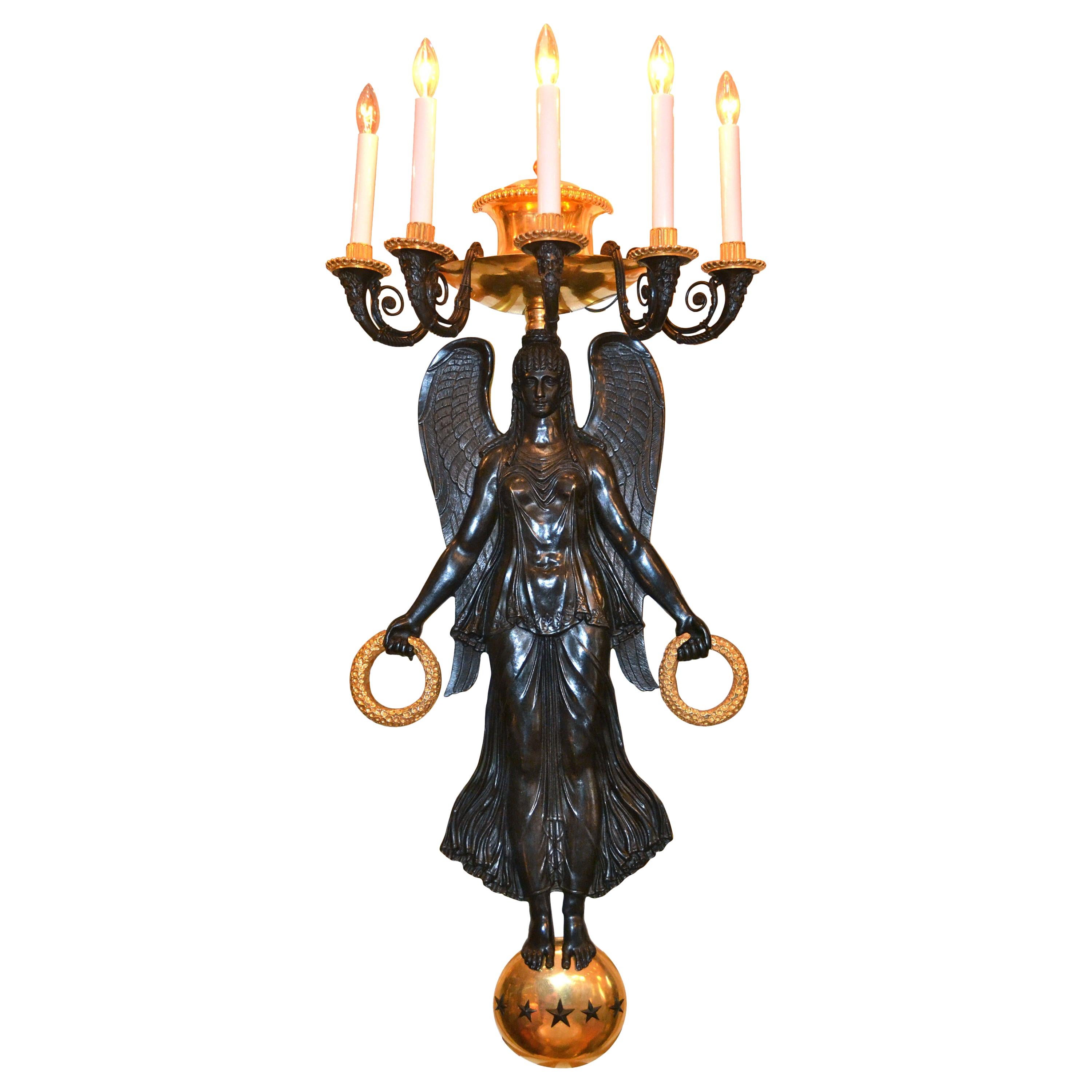 A very large and dramatic pair of French Empire style wall sconces in finely chased patinated and gilded bronze. A large winged Victory in high relief stands on a gilded globe studded with stars. She holds a gilded wreath in each outstretched hand,
