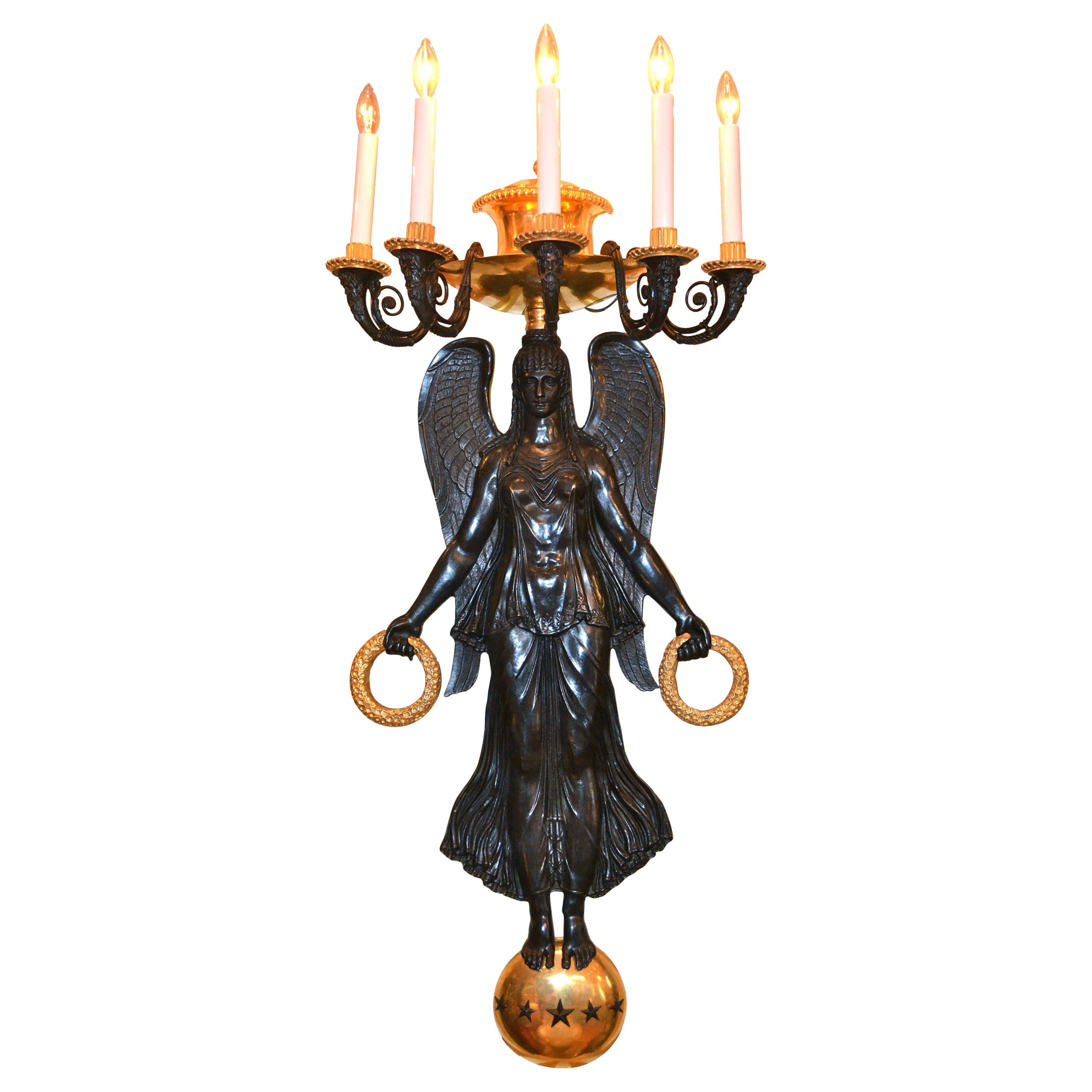 Una coppia di appliques in stile Impero francese, molto grande e scenografica, in bronzo patinato e dorato finemente cesellato. Una grande Vittoria alata in alto rilievo si erge su un globo dorato tempestato di stelle. Tiene una corona dorata in