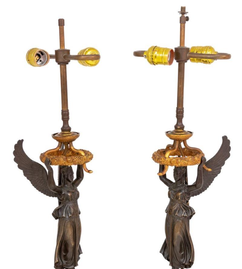 Coppia di lampade figurative in bronzo dorato e patinato dell'Impero francese, circa 1830 e montate successivamente, ciascuna con una figura di Vittoria in piedi che sostiene una corona di fiori, su un piedistallo cilindrico affusolato e un