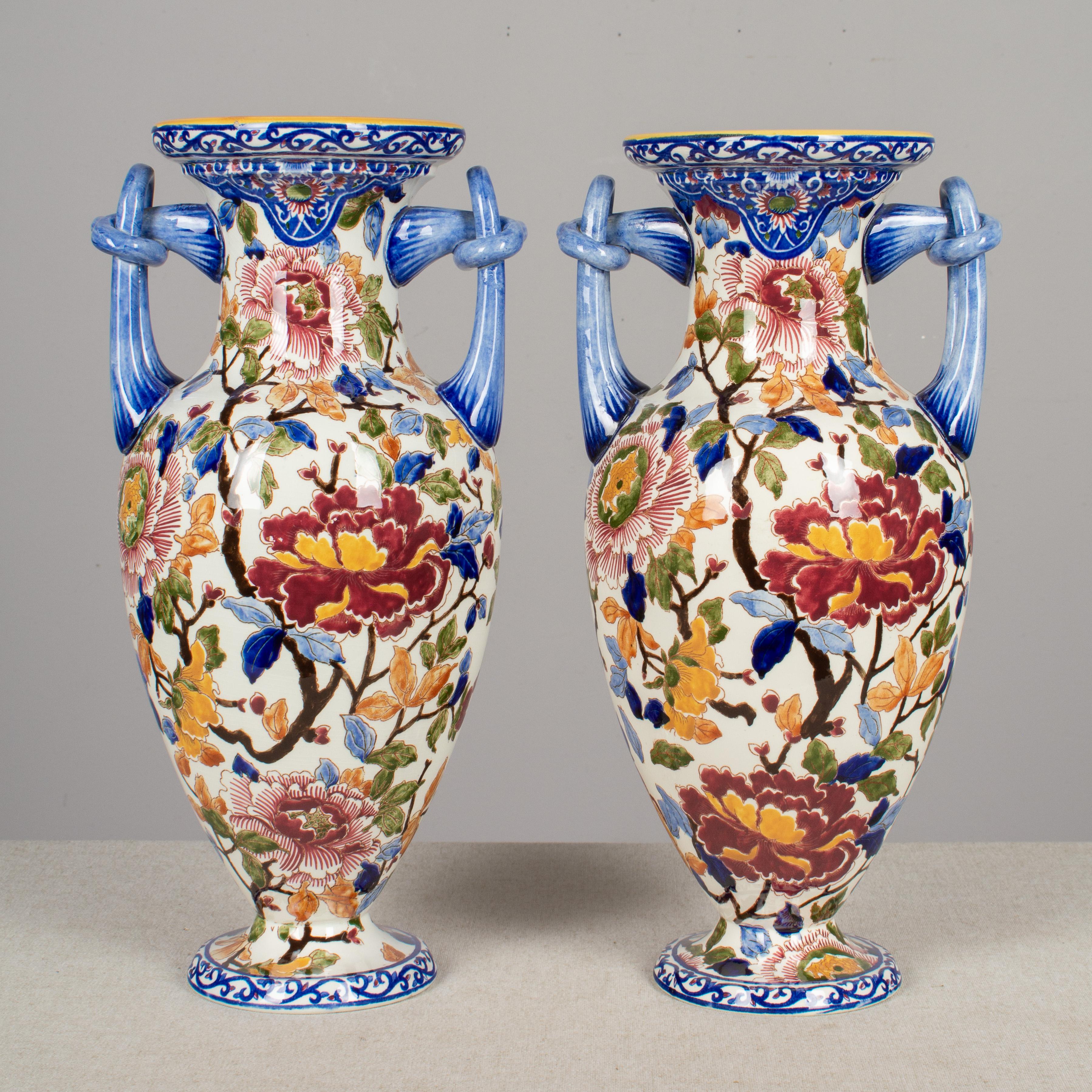 A superb pair of faience French vases from Gien with hand-painted floral pattern in bold vivid colors. Flared baluster shape with blue double handles. Marked on the underside. Overall: 15.5