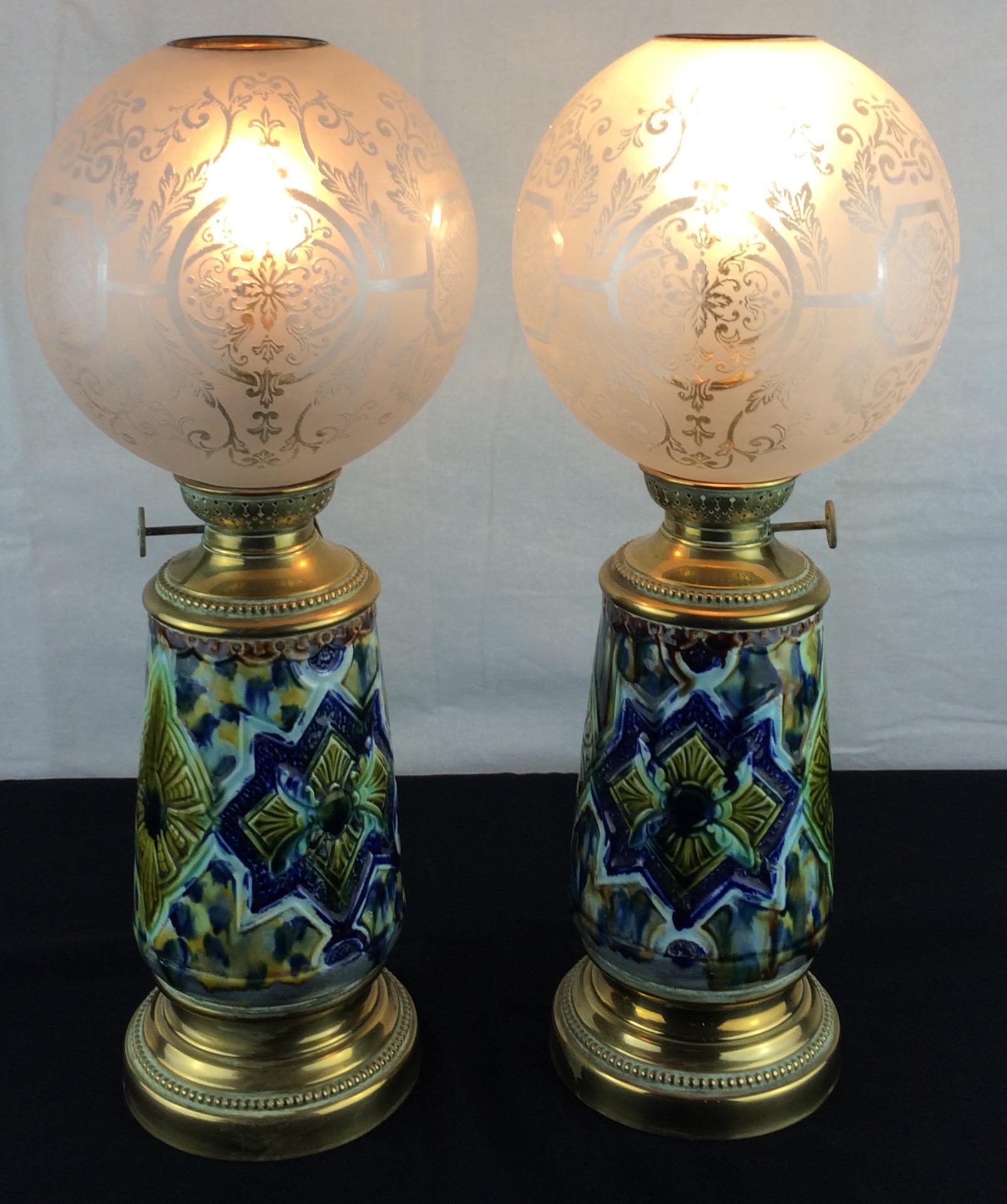 A wonderful pair of table lamps converted from oil lamps and electrified. 

The lamps feature swirl-patterned glass ball shades. These cover the burners, which top gilt brass pierced collars with wick-raiser handles. The lamps’ faience bodies are