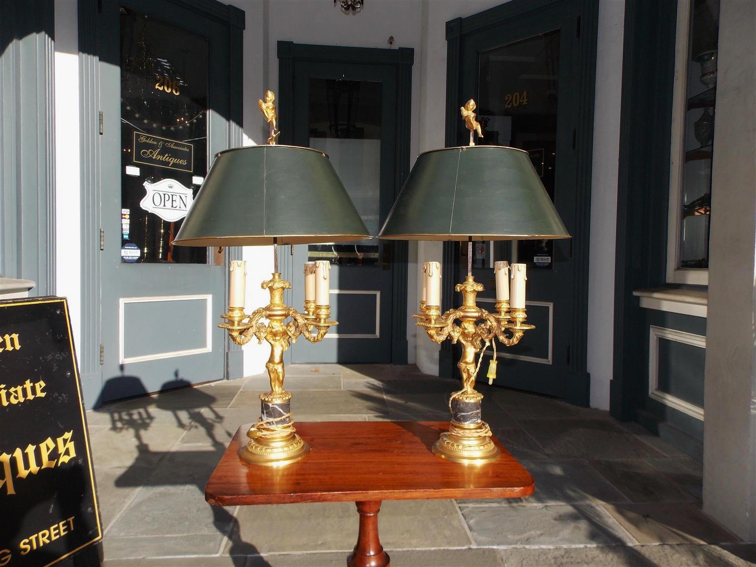 Pair of French gilt bronze figural Bouillotte lamps with hand painted adjustable tin shades, decorative locking arrows, four-light interior clusters, and resting on circular gilt bronze beaded marble bases, Mid-19th century. Lamps were originally
