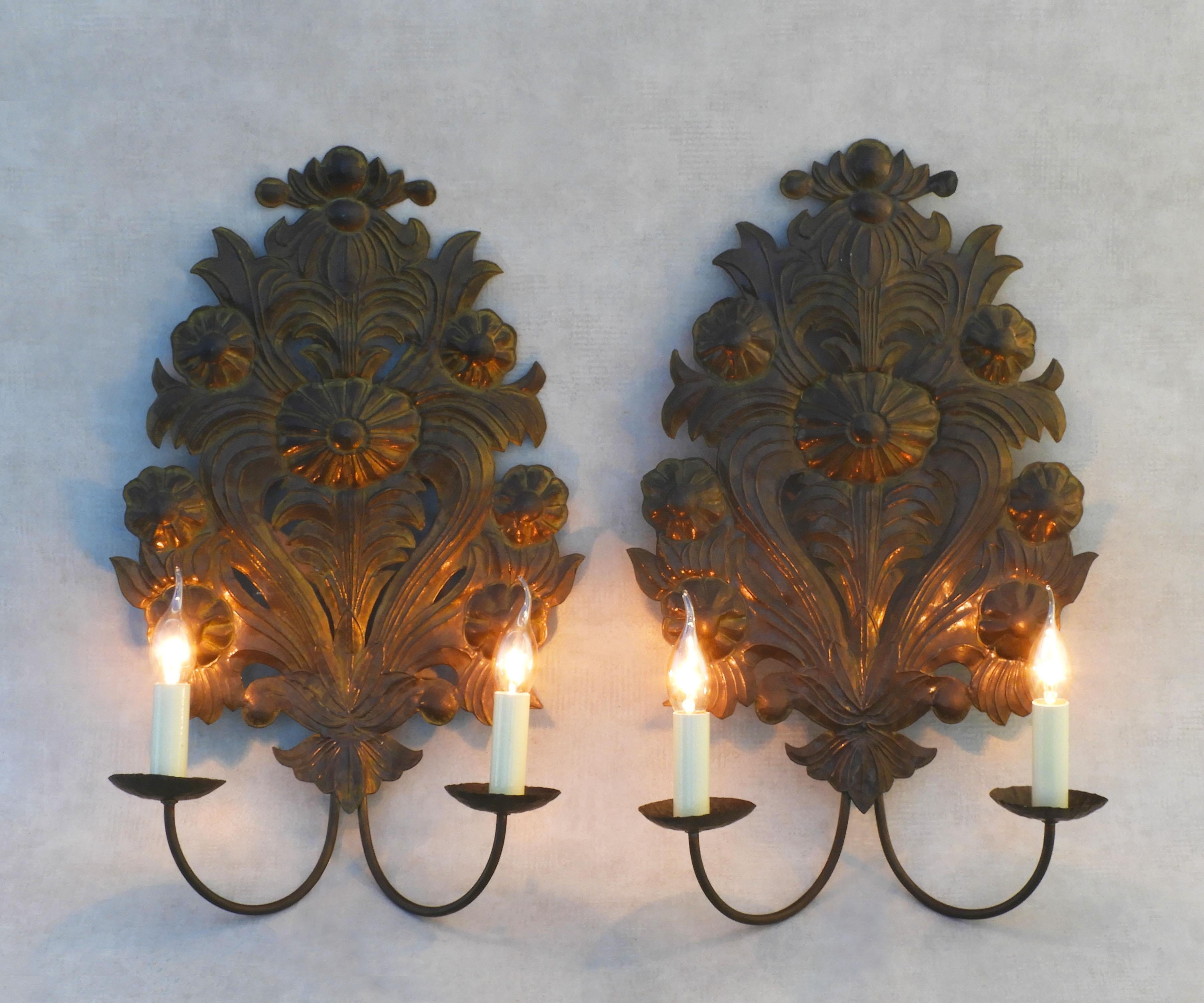 A pair of large, tôleware repoussé wall light sconces from early 20th Century France. 
Two ‘grand appliqués’ in hand-embossed brass tôle, each with two faux candlelights. More recently converted for electricity, these sconces would have been