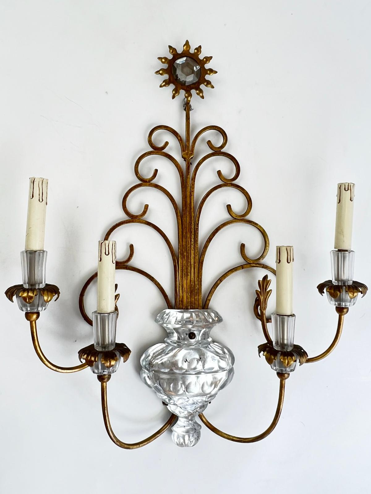 Pair of sconces, in the style of Maison Bagues, each having four, C-scroll candlearms, extending from a silvered, cut glass urn, ending in glass candlepots and electrified candles over foliate-draped glass bobeches. Each backplate of five graduated