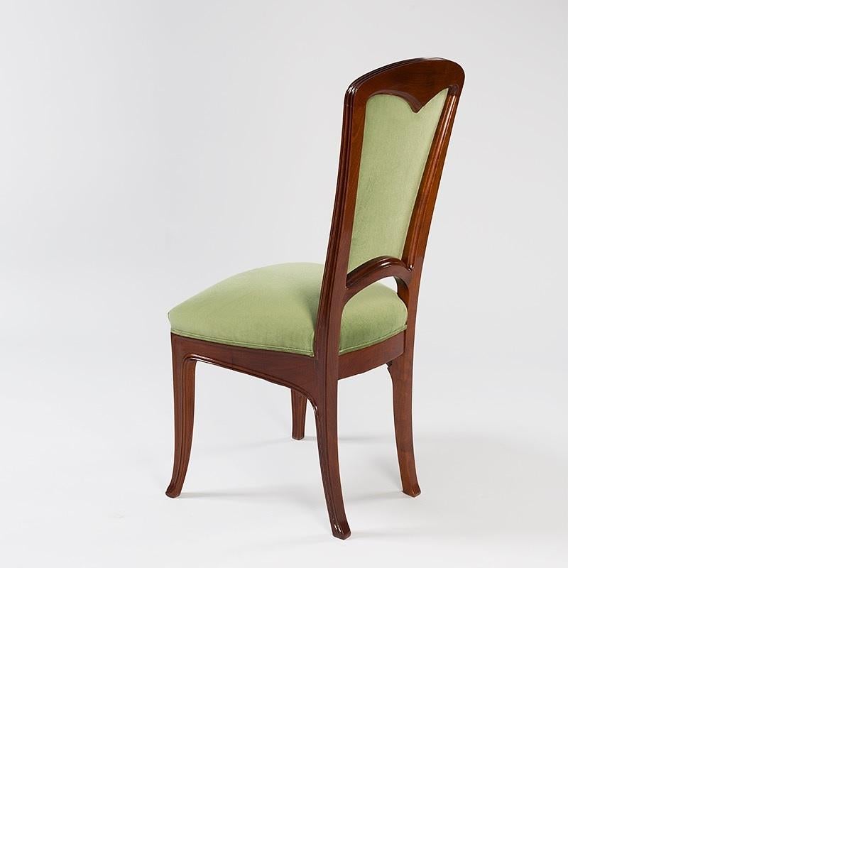 A pair of French side chairs in mahogany by Camille Gauthier & Paul Poinsignon. The chairs have carved stylized flowers on their backs, arms and below the seats. They are upholstered in green fabric.