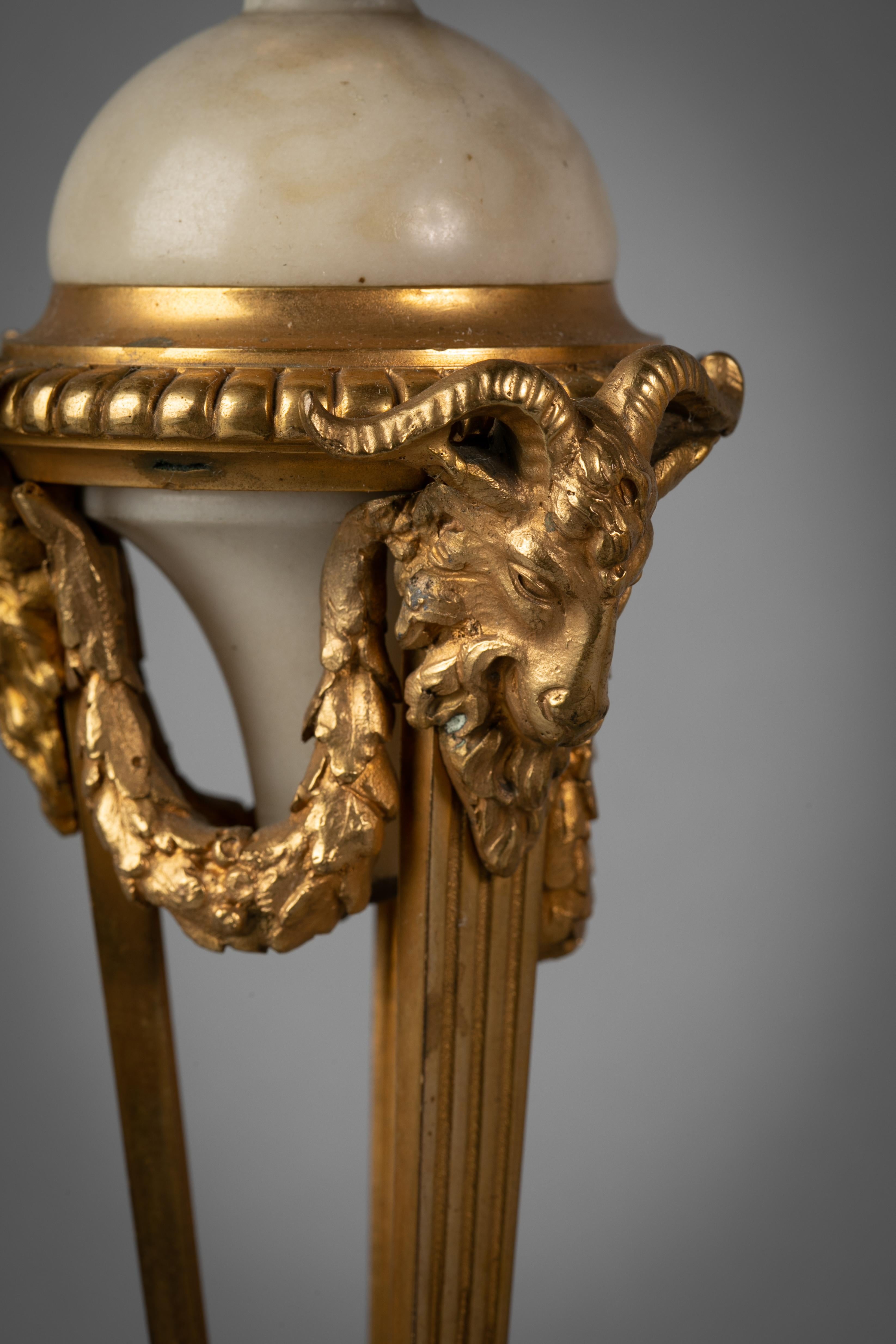 Pair of French gilt bronze and marble covered urns with flame finial, ram's head and hoofed feet.