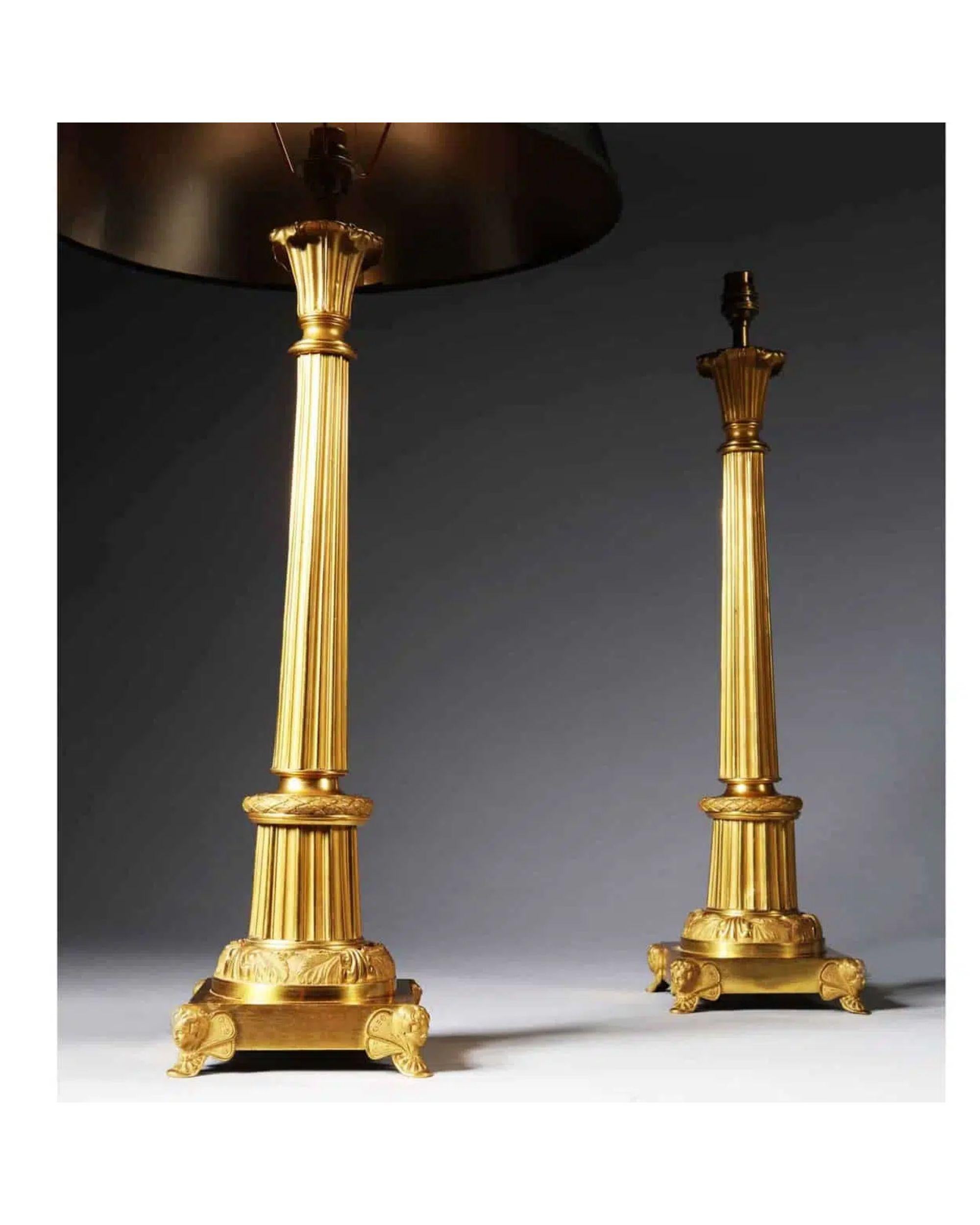 Pair Art Deco gilt bronze and tole antique gold column table lamps.

Standing on square bases supported on winged cupids, the tapering fluted column with burnished gold highlights on a stepped circular foliate bronze mount and surmounted by a