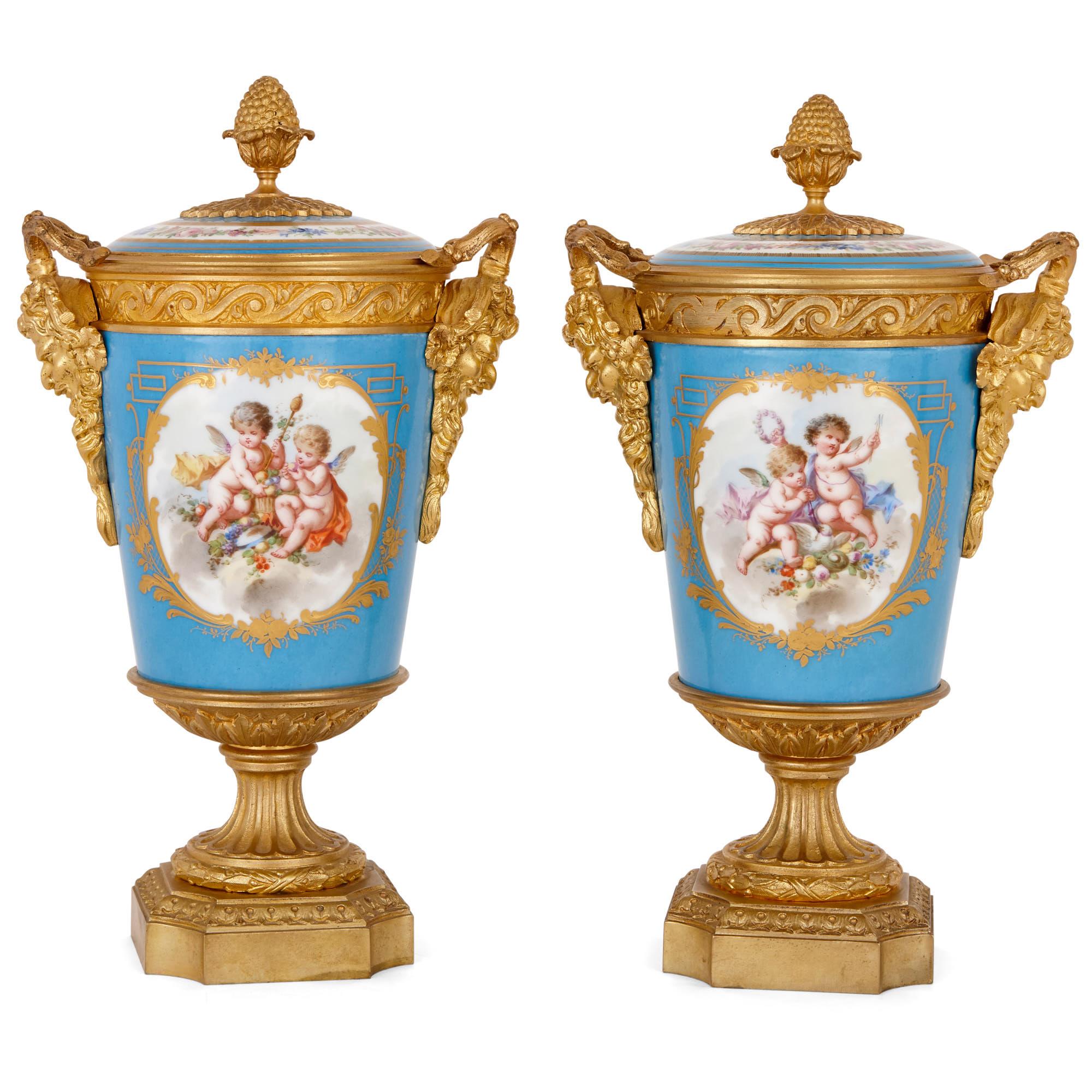 These beautiful porcelain vases feature elegant Rococo-style decorations in the manner of the Sèvres manufactures. 

The vases feature slightly flared cylindrical porcelain bodies which are topped by shallow domed porcelain lids. The lids are