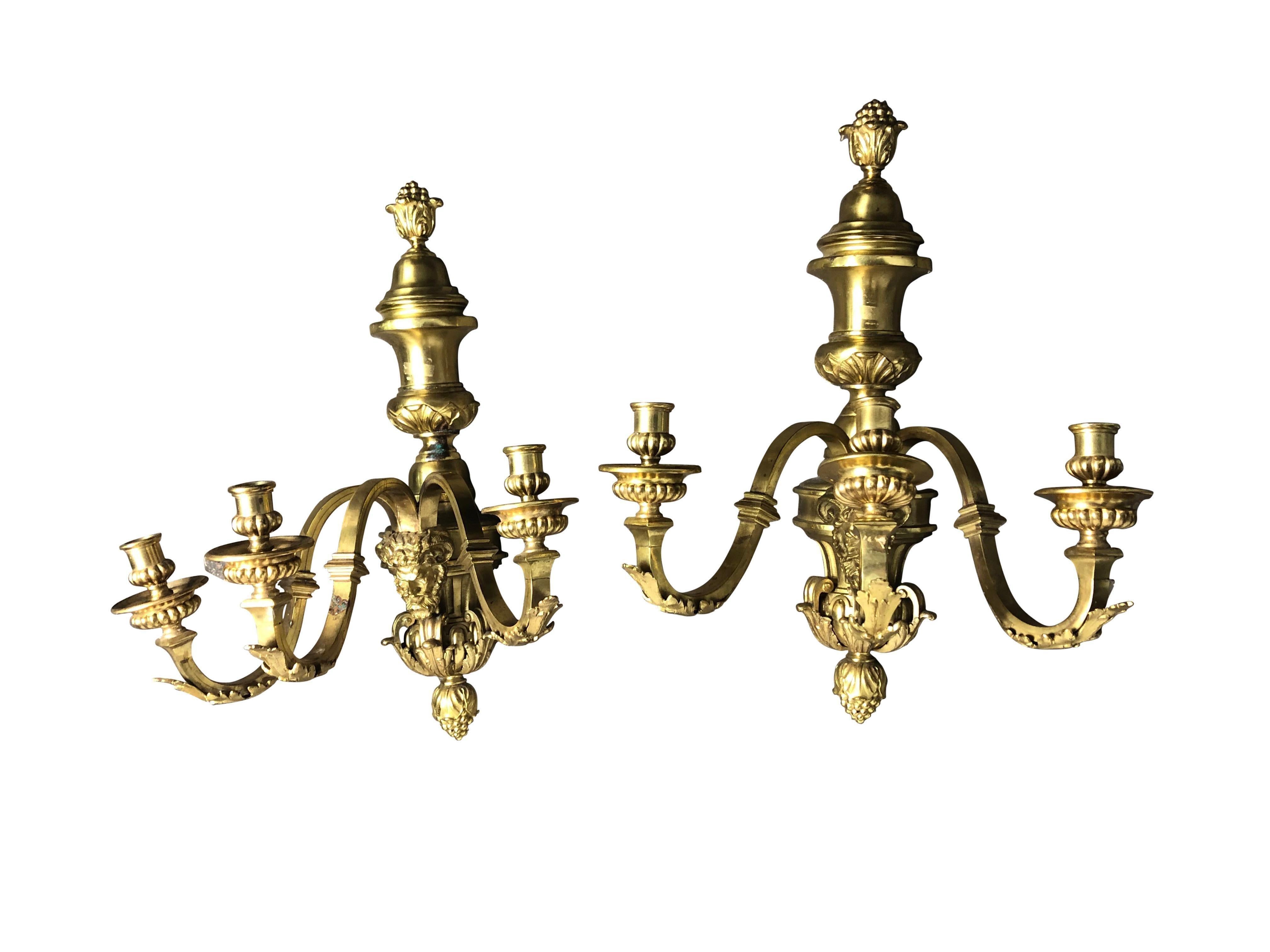 A Pair of French large and heavy gilt bronze three-light sconces, each with a classical man's face. Fleur-de-lis bracket design. Fine quality casting and bright polished gold patina with lacquered finish. Small areas of aged patina which add to the