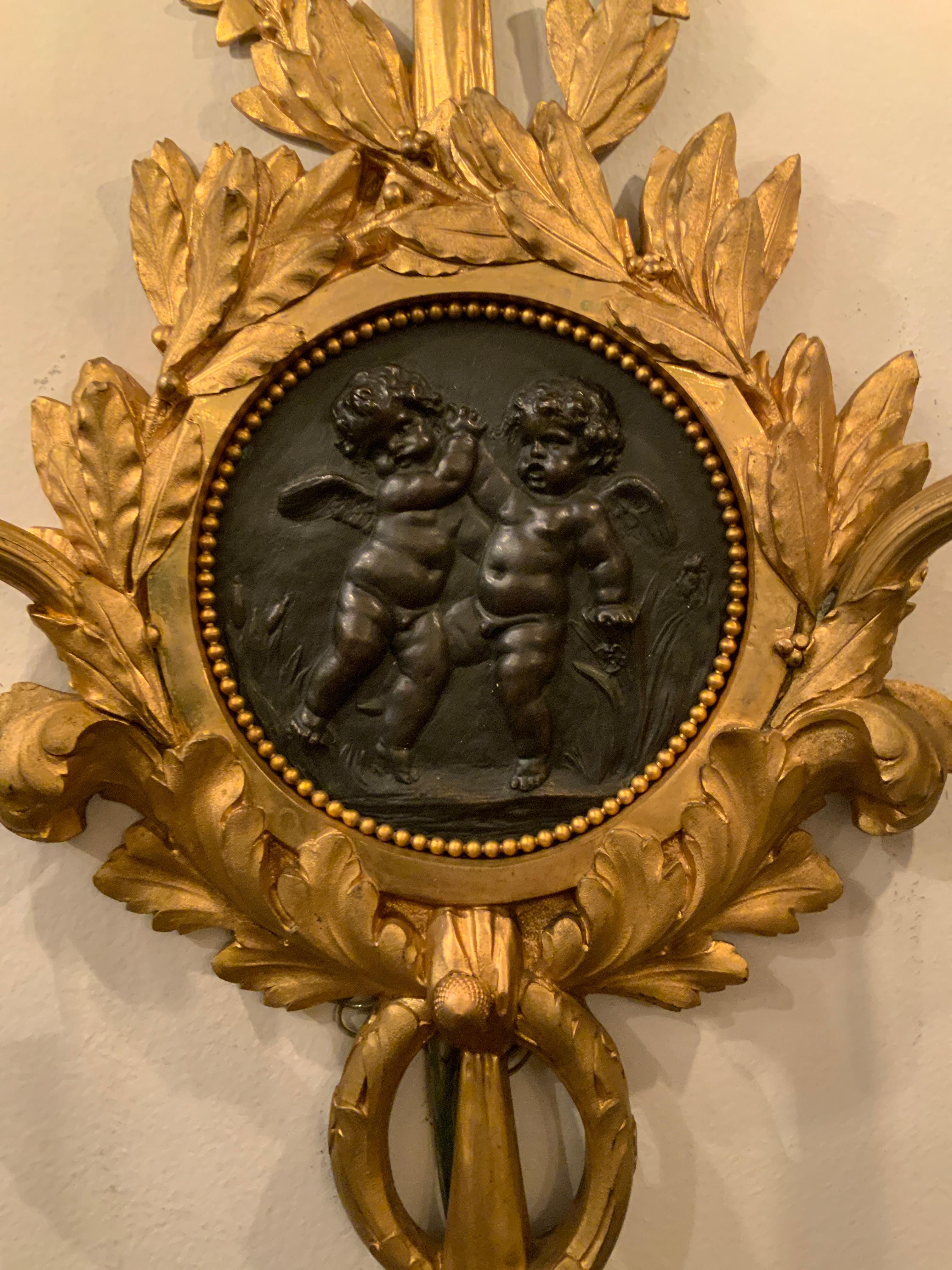 Paire d'appliques à trois lumières avec bras à volutes,
Français, motif de putti au centre de l'avant avec des feuillages.
et la conception des rubans. Câblé.