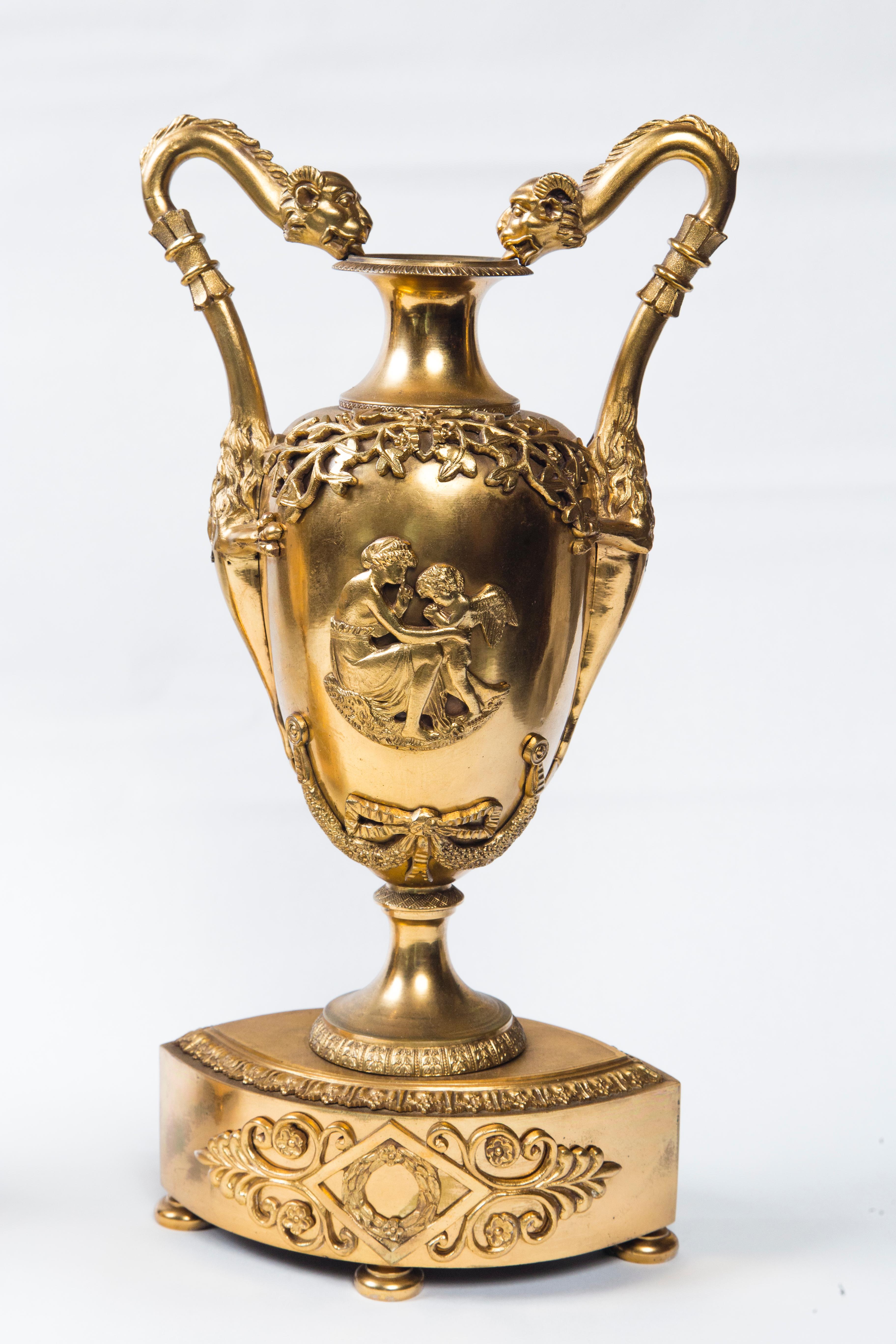 Dating from the early 19th century this pair of sealed top urns have extending dragon heads with rams horns neck handles, hairy mid body with extended 3 toed claw feet grabbing the urn, and ending in arrow pointed tails. Each is decorated with
