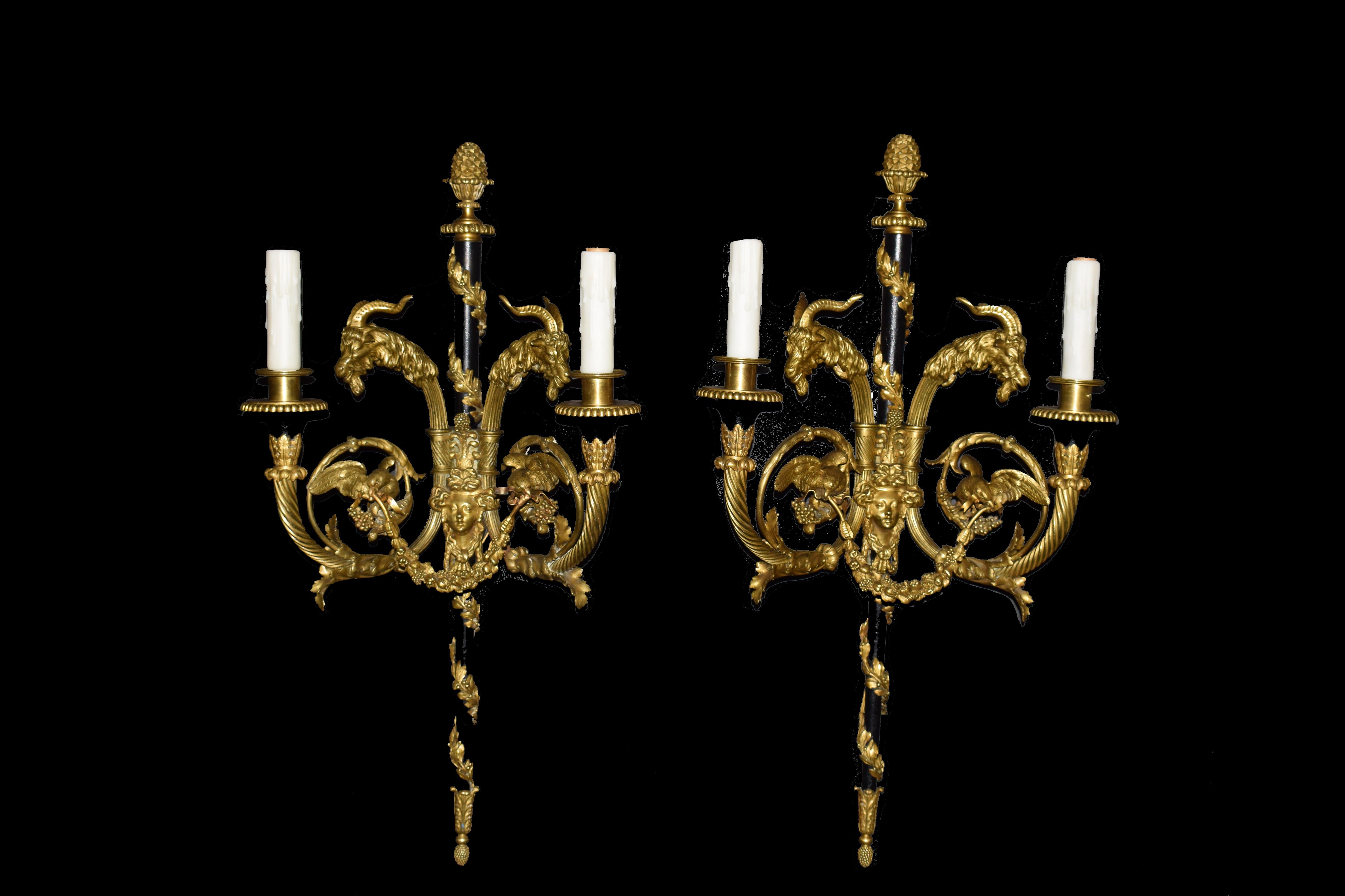 Paire d'appliques à deux lumières en bronze doré et émaillé signées Millet a Paris. Dans le goût néoclassique, les sceptres se terminant par des fleurons en artichaut, les bras en chandelle moulurés sertis de têtes de bélier et d'oiseaux, un masque