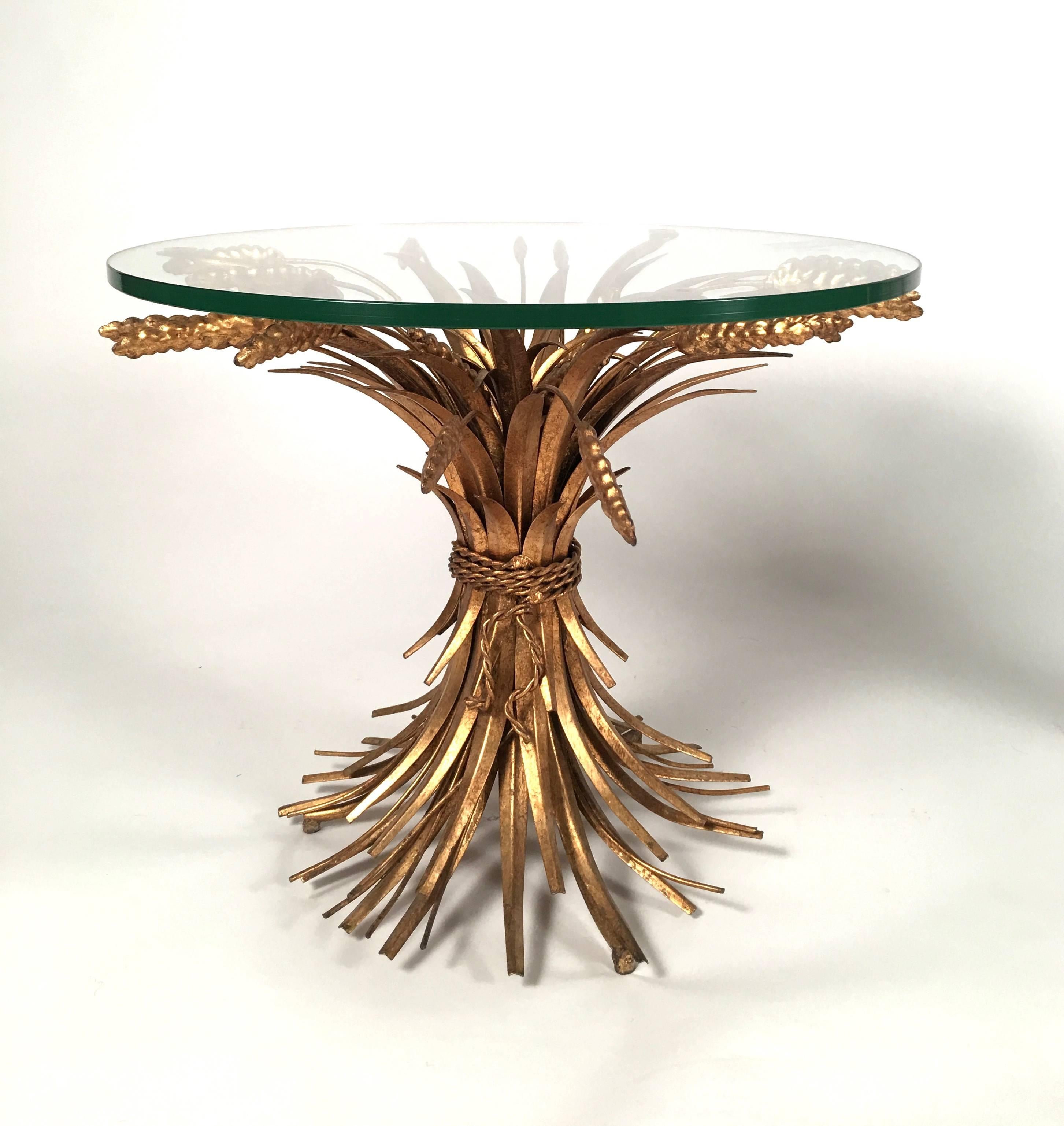 A stylish pair of French ribbon tied sheaf of wheat tables in well patinated gold metal, with new tempered glass round tops. 
These tables became famous when Coco Chanel decorated her apartment at 8, rue Cambon, Paris, with a similar example,