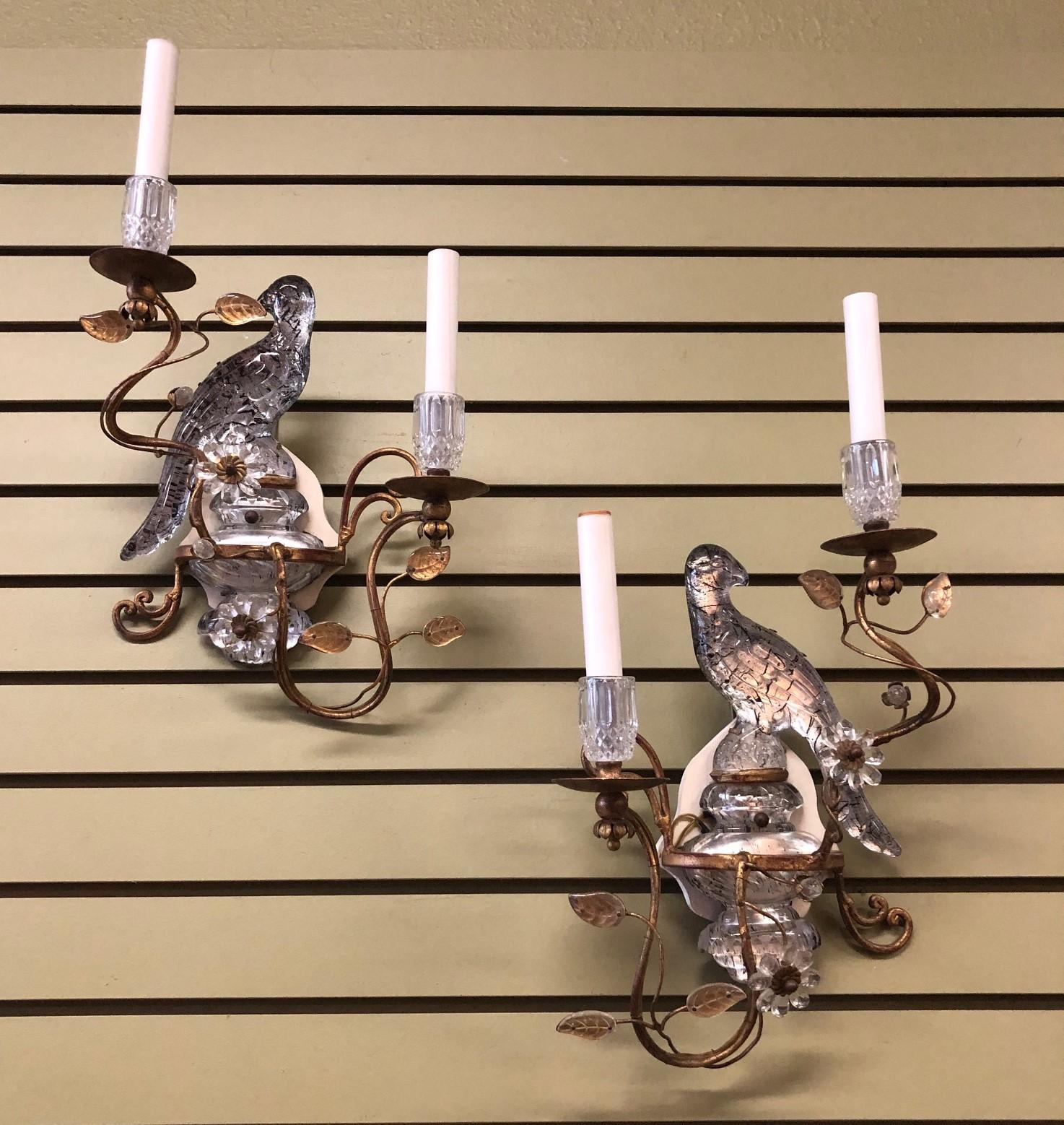 Pair of French Hollywood Regency style gilt sconces with parrots by Maison Bagues, circa 1950s. The sconces feature decorative glass parrots and surrounding floral motifs against gilt metal. Excellent condition, restored and rewired to US standard.