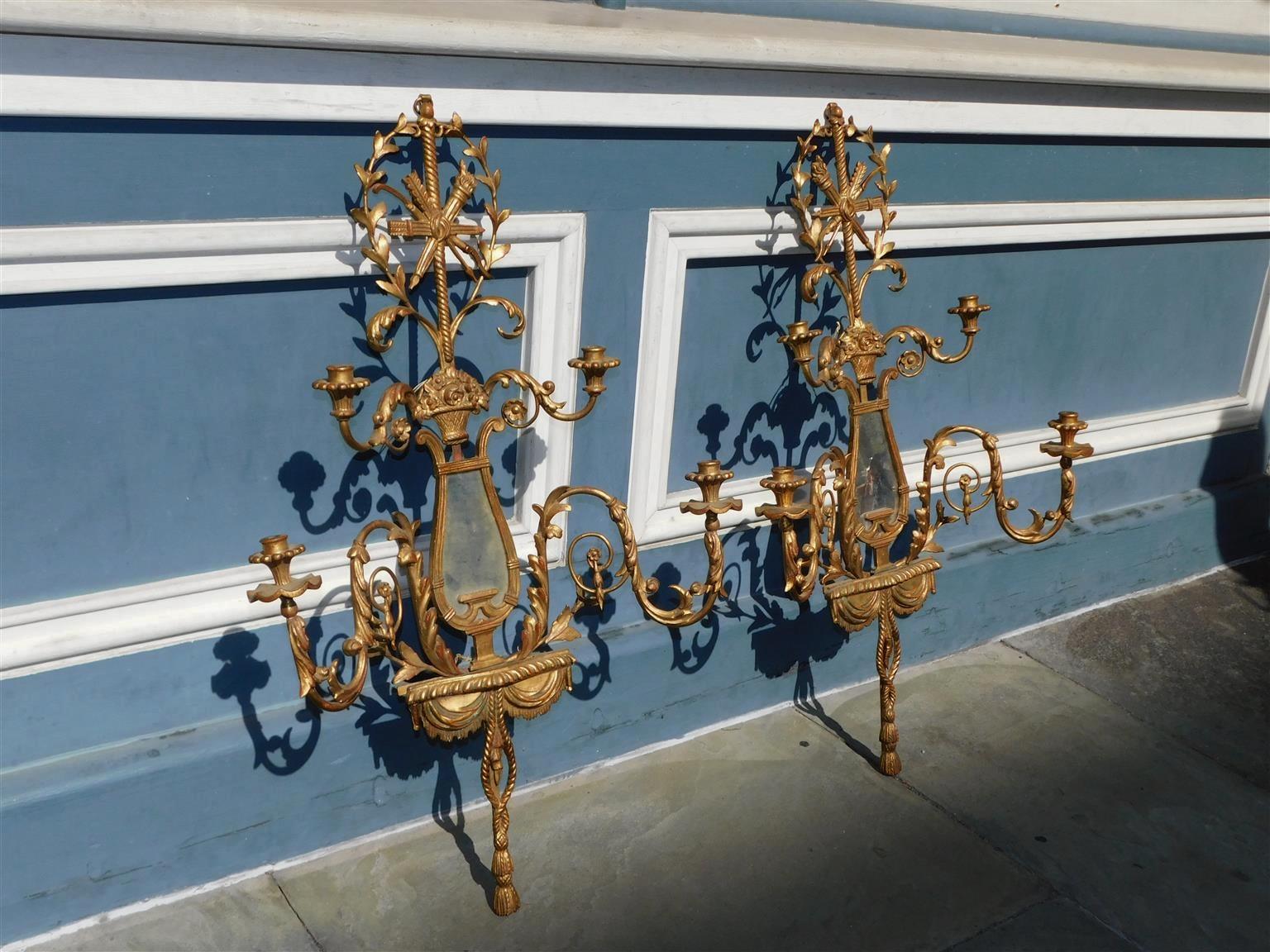 Pair of French gilt wood and Gesso wall sconces with torches and arrows, centered flower basket, four scrolled acanthus medallion arms, flanking harp mirrors, and valences with rope tassels. Early 19th Century. Sconces retain the original mirrors