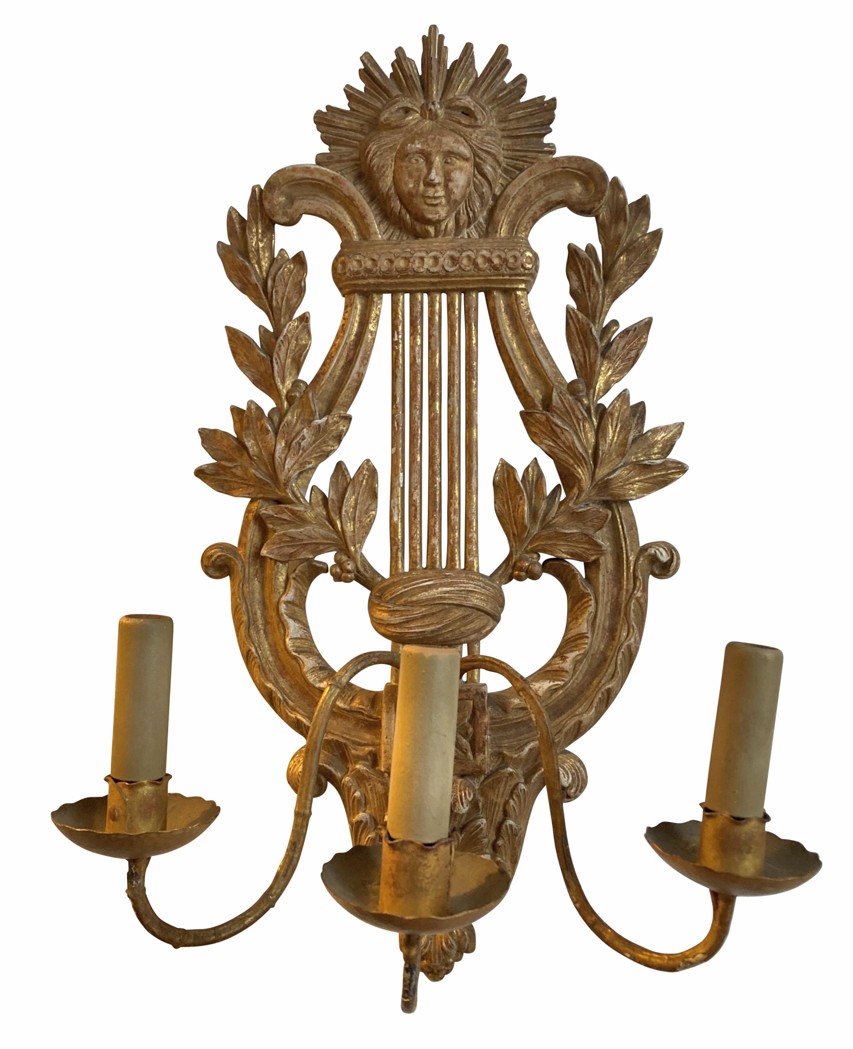 A pair of French carved giltwood three branch wall sconces with lire backs, laurel and mask decoration.