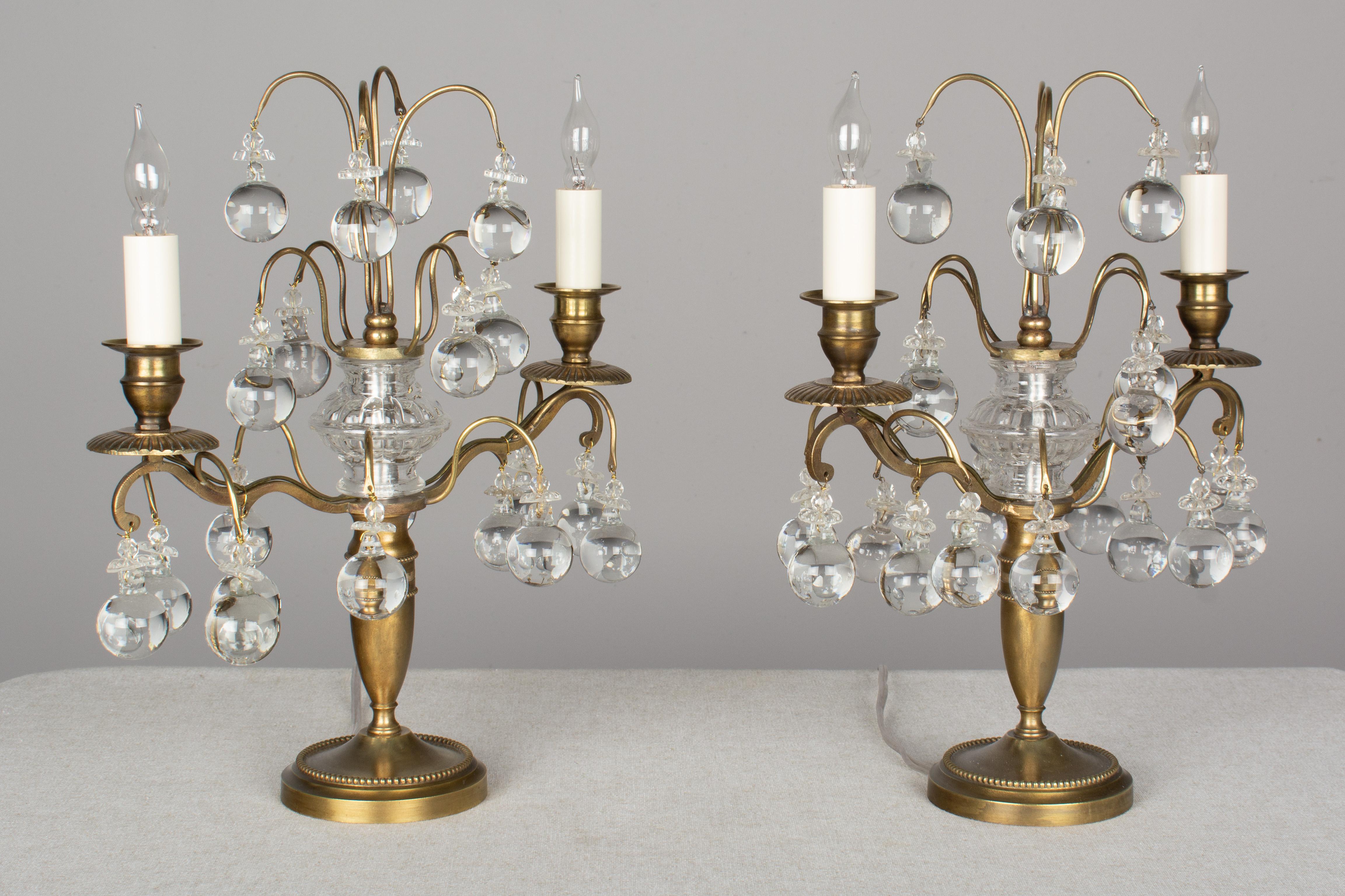 A pair of French two-light girandoles made of brass and decorated with crystal balls, rosettes and faceted beads. New candle covers. Rewired with new sockets and in working order. Base: 4