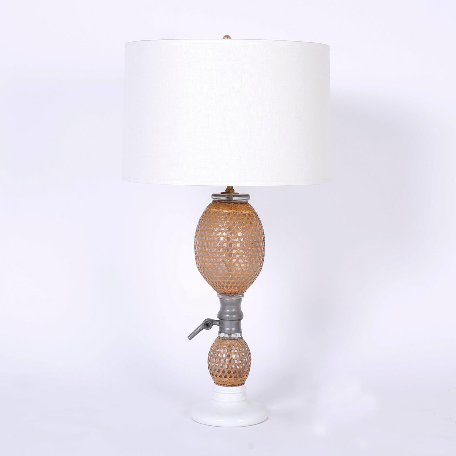 Pair of antique French bottles with serving spouts now serving as table lamps composed of hand blown glass wrapped in wicker with pewter hardware and white porcelain bases.