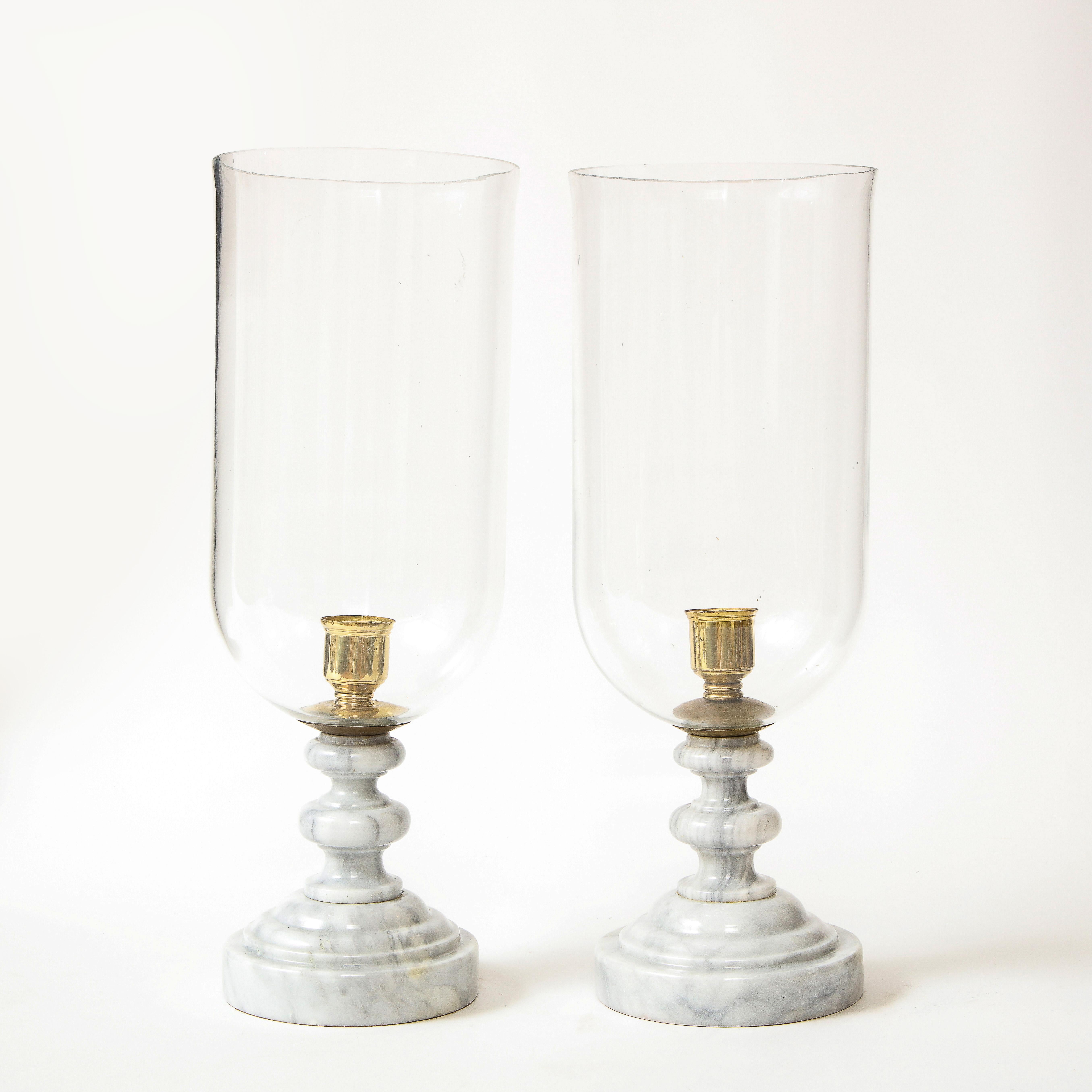 Each with a glass hurricane shade mounted on a turned polished marble base.