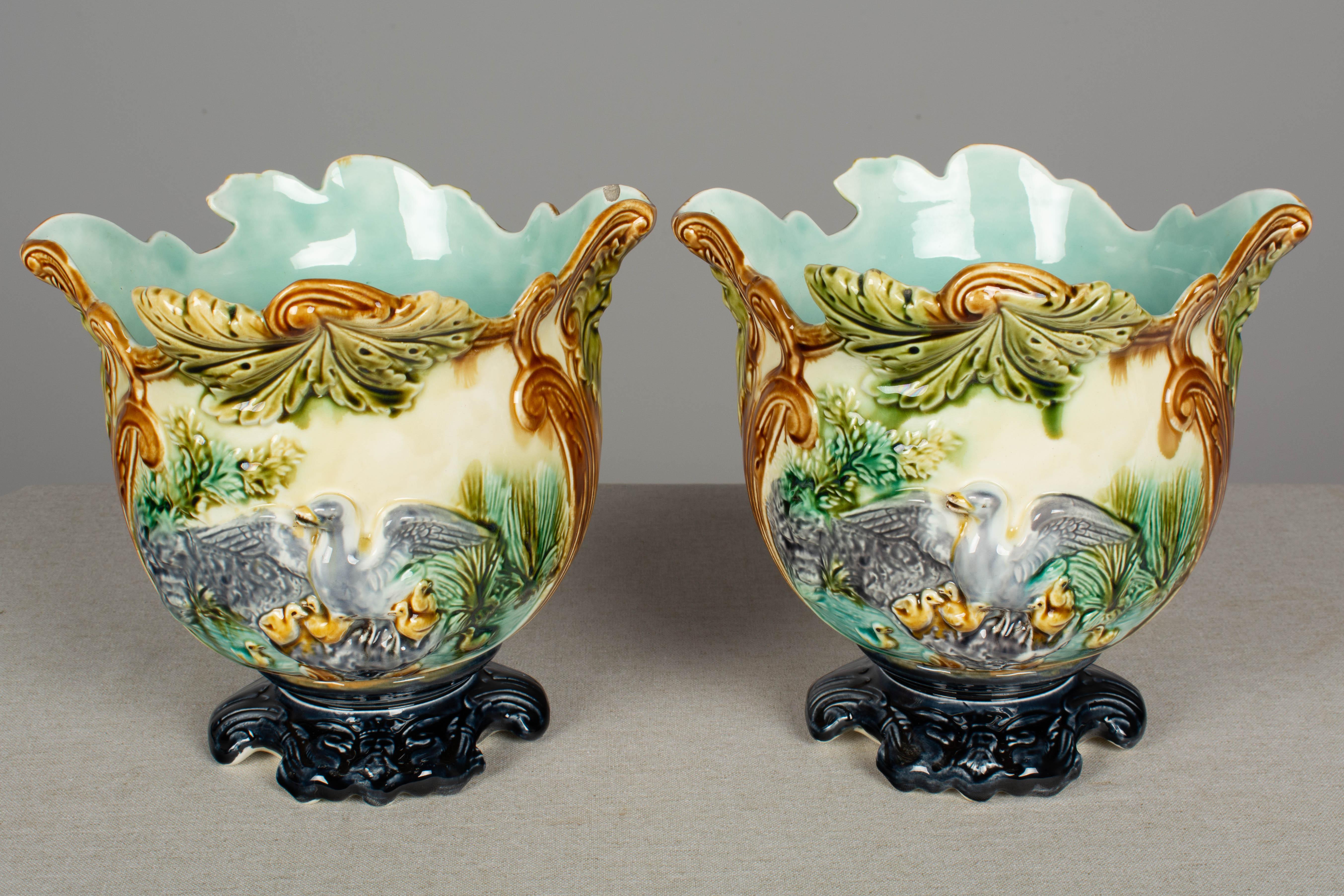 A pair of French Majolica cache pots, or planters, each depicting a duck with wings outstretched over a family of ducklings. Rich coloring of green, brown, ocher and grey with aqua interior and dark blue base. Minor chip to glaze of the interior of