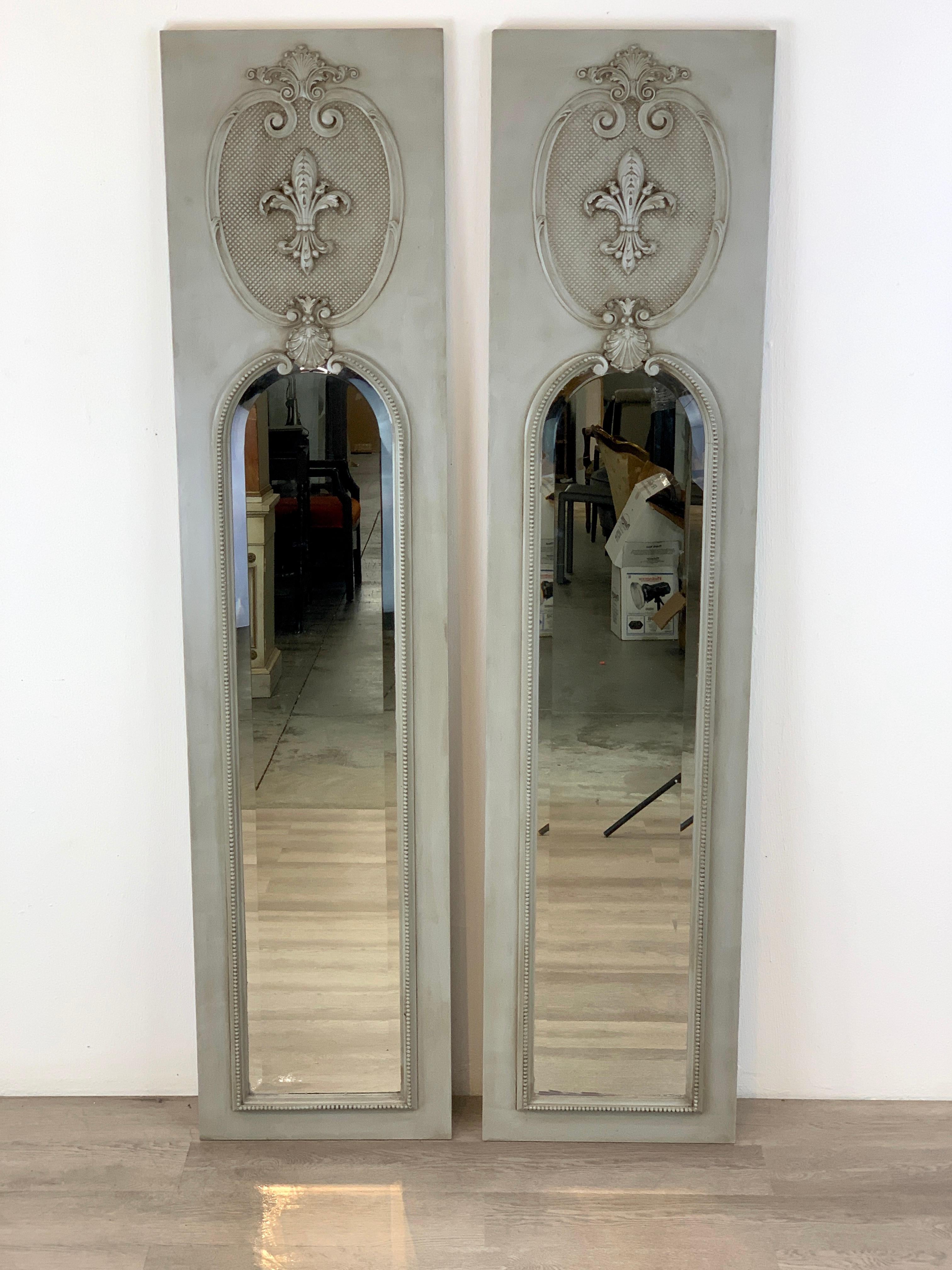 Pair of French grey panted trumeau mirrors, each one with carved fleur de lis cartouche, the lower inset beveled mirror measures 47
