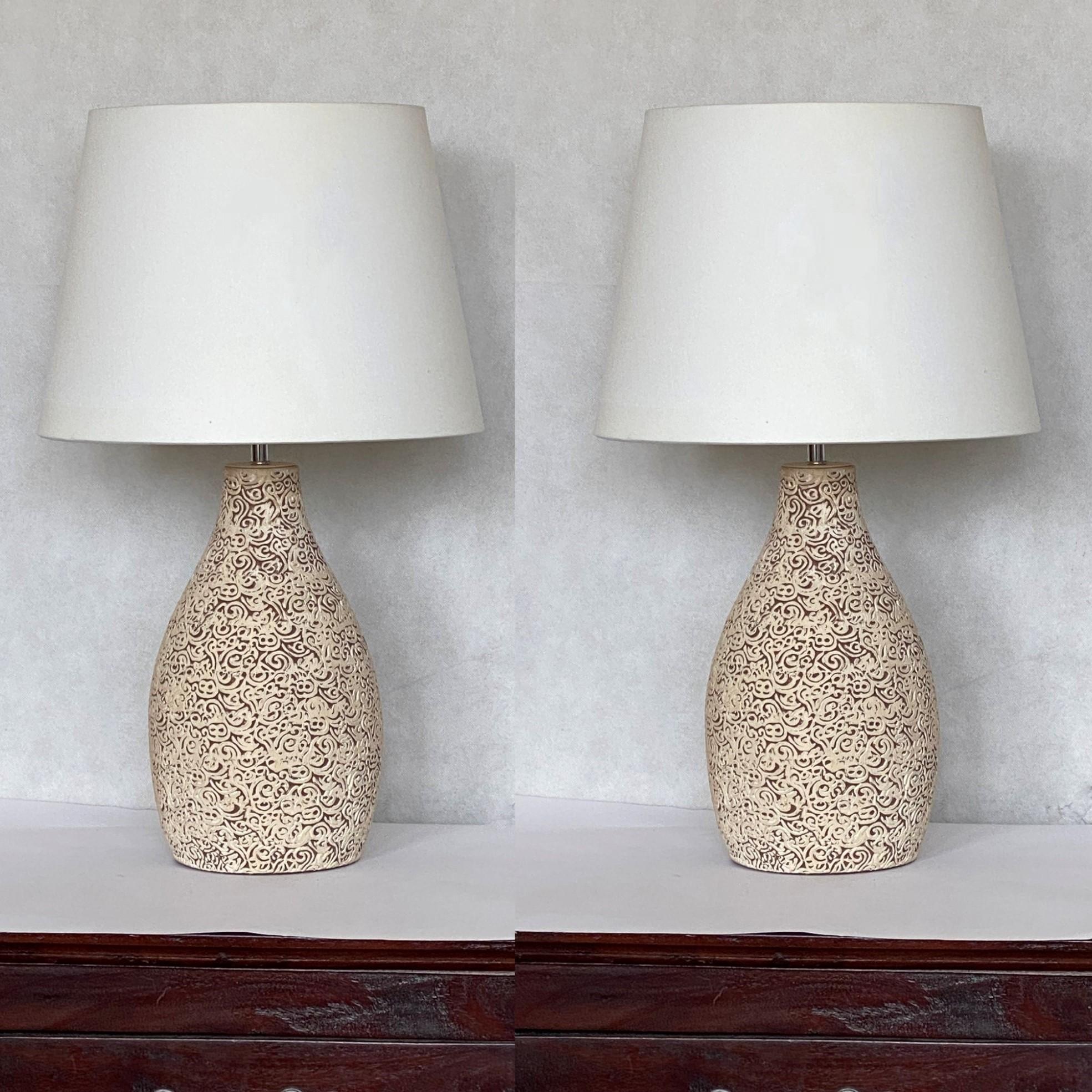 A pair of French ceramic vase table lamps. Hand-crafted round ceramic body in structured organic form with new fabric lamp shades, France, 1960s. Both lamps in fine vintage condition, no damages, rewired, new shades. Switch to turn on and off on