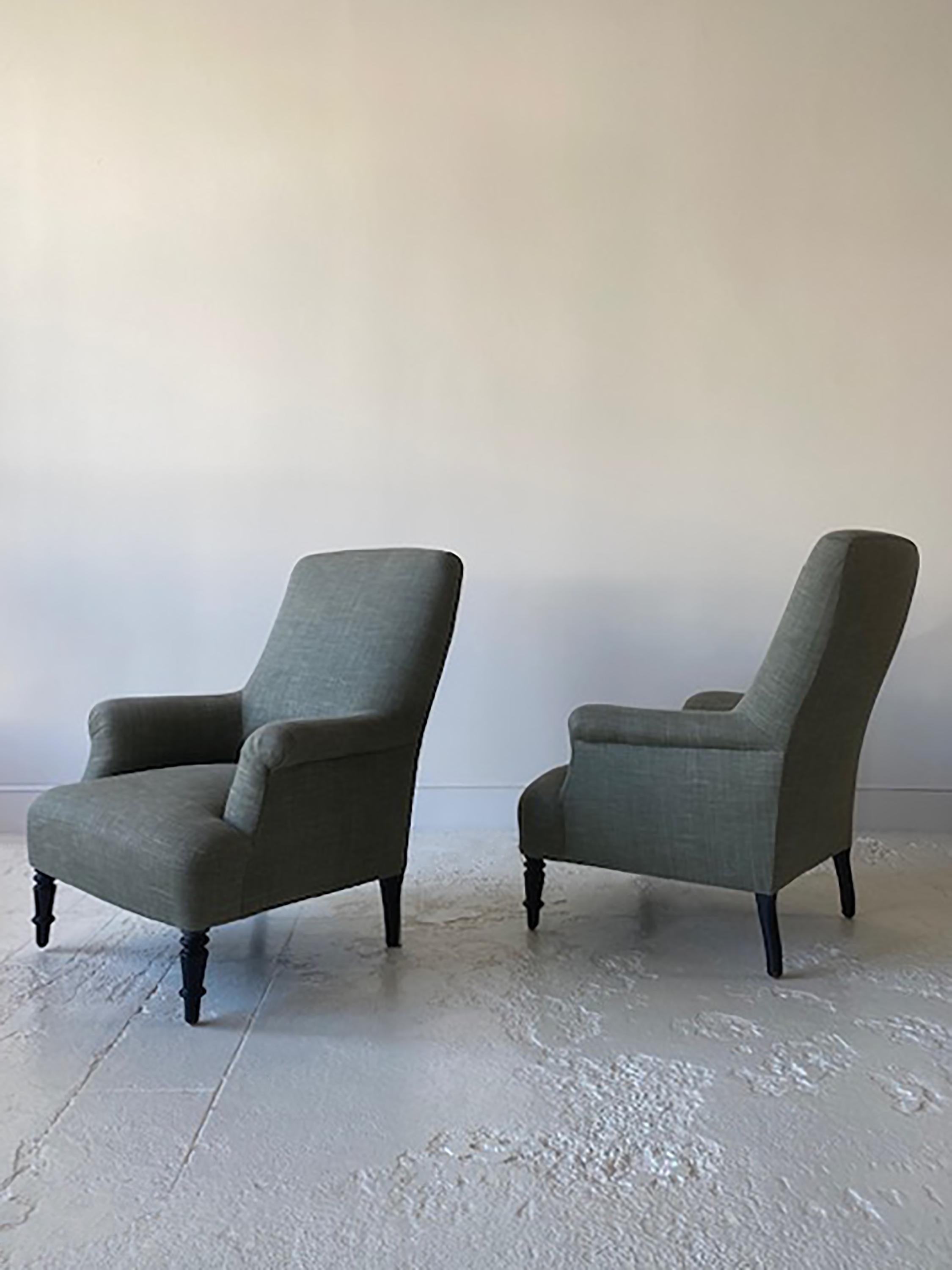 Pair of classic French high back club chairs with rolled arms, newly upholstered in a faded green linen fabric. Original leg finish intact to keep an aged patina presence to the chairs.